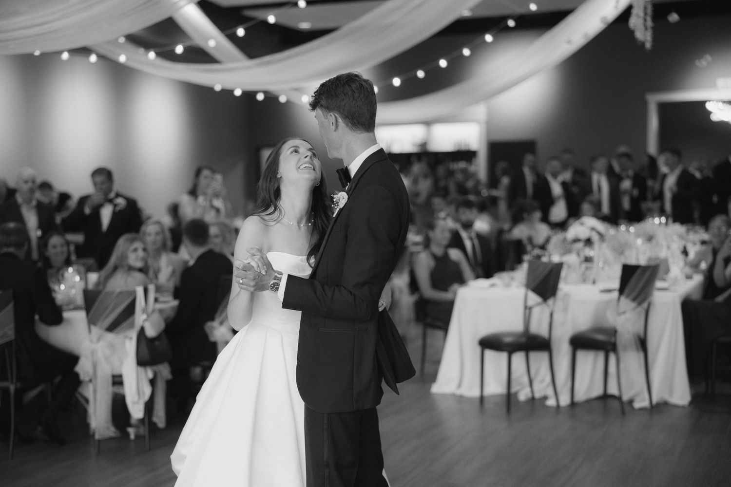 Black and white photo of a bride and groom sharing their first dance at a wedding reception.