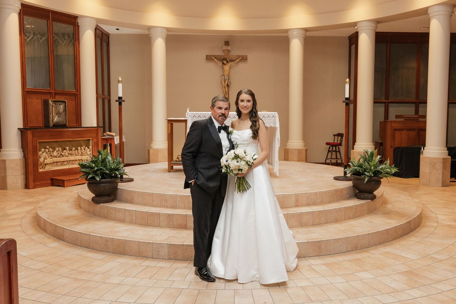 Bride and groom posing together at church altar after wedding ceremony with crucifix and columns in background.