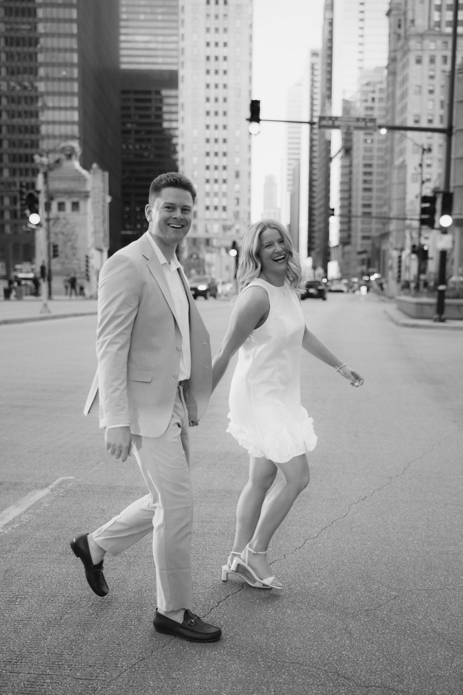 Black and white photo of a laughing couple holding hands while crossing a city street.