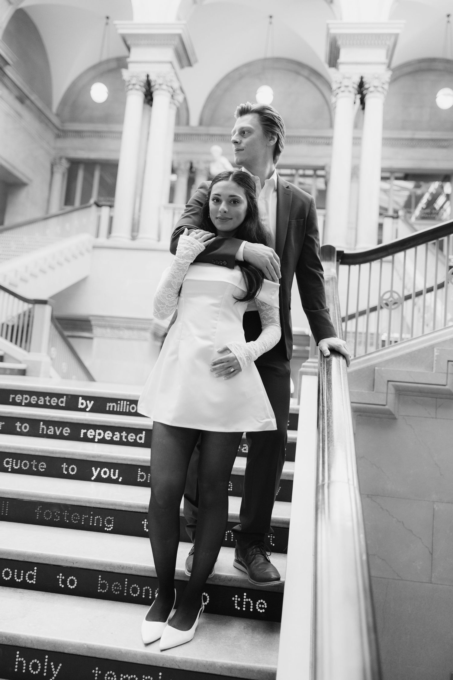 Couple embracing on elegant staircase with text overlays in background.