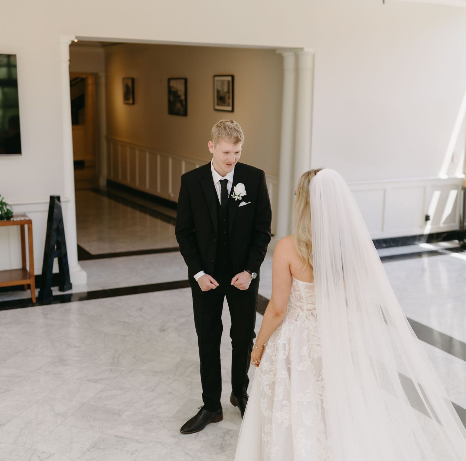 A bride and groom share a tender first look moment in an elegant white hallway during their wedding day.