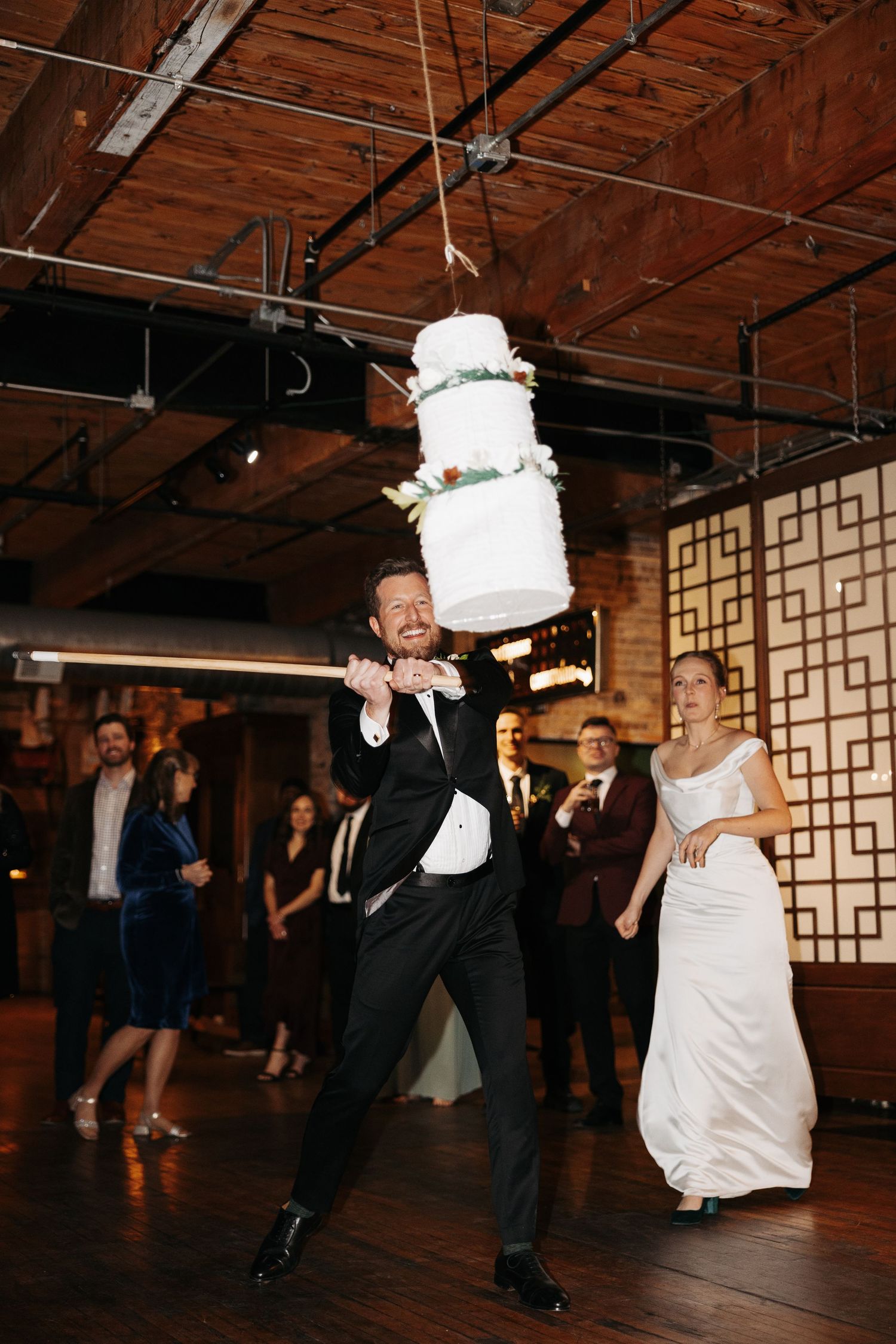 A bride and groom perform a playful cake smash dance sequence at their wedding reception in a rustic venue.