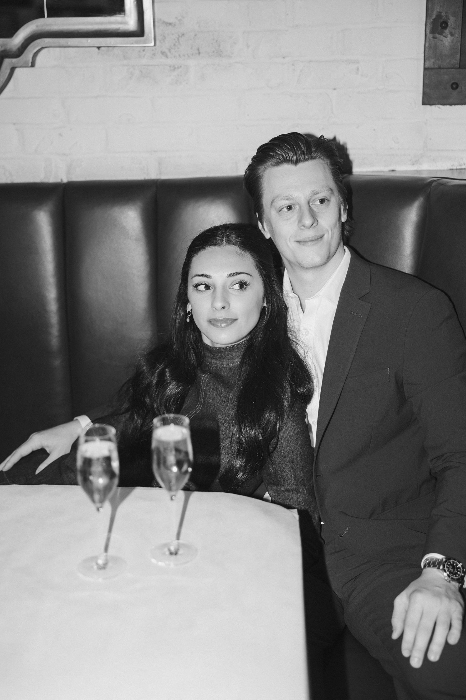 Couple enjoying drinks together at an elegant restaurant booth in formal attire.