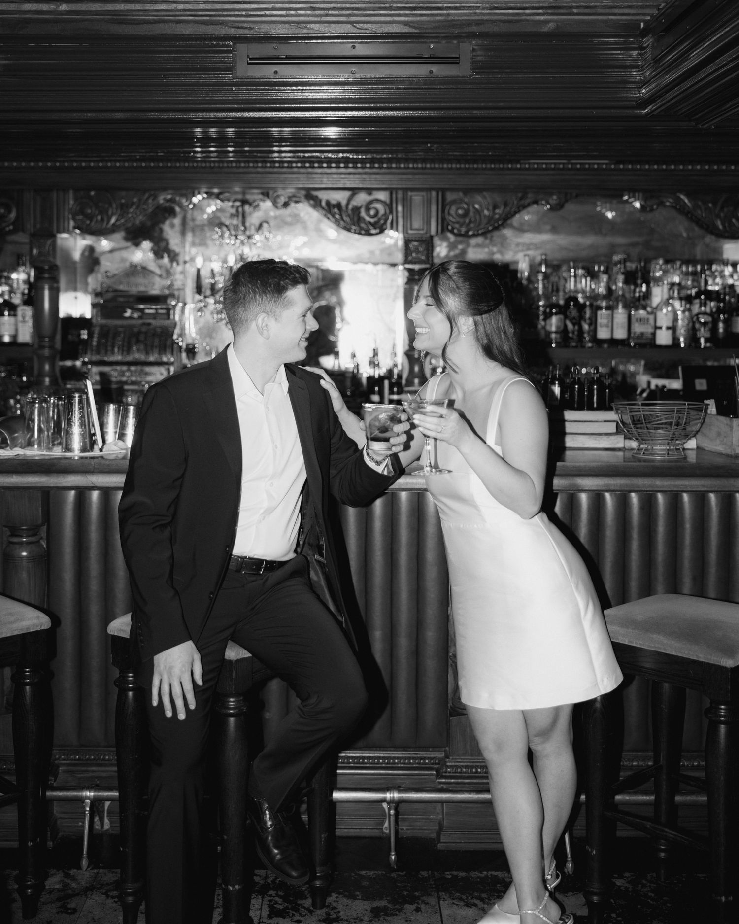A couple in formal attire sharing drinks at an elegant vintage bar in black and white.
