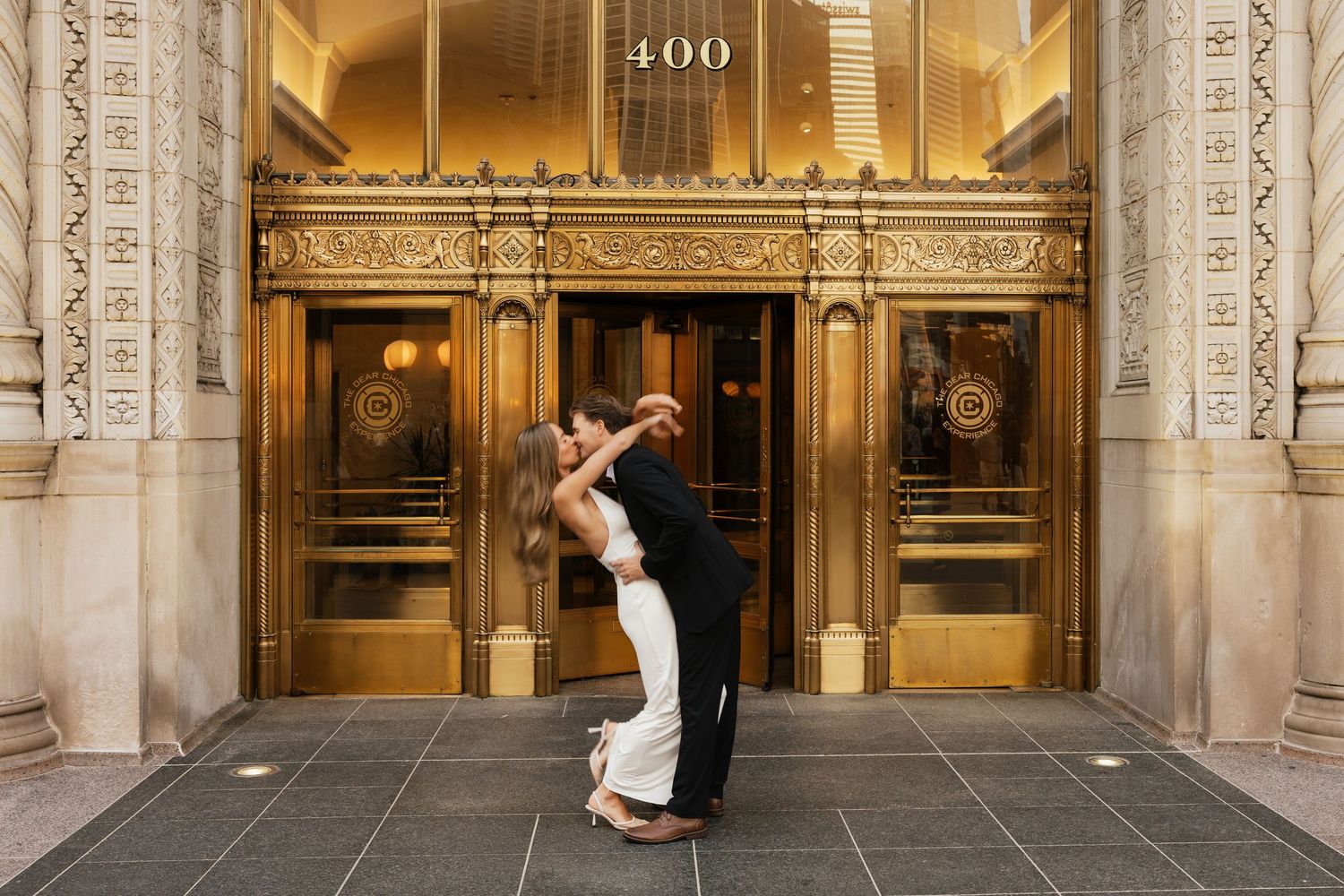 Couple sharing a romantic dip kiss in front of elegant gold entrance doors at 400 building.