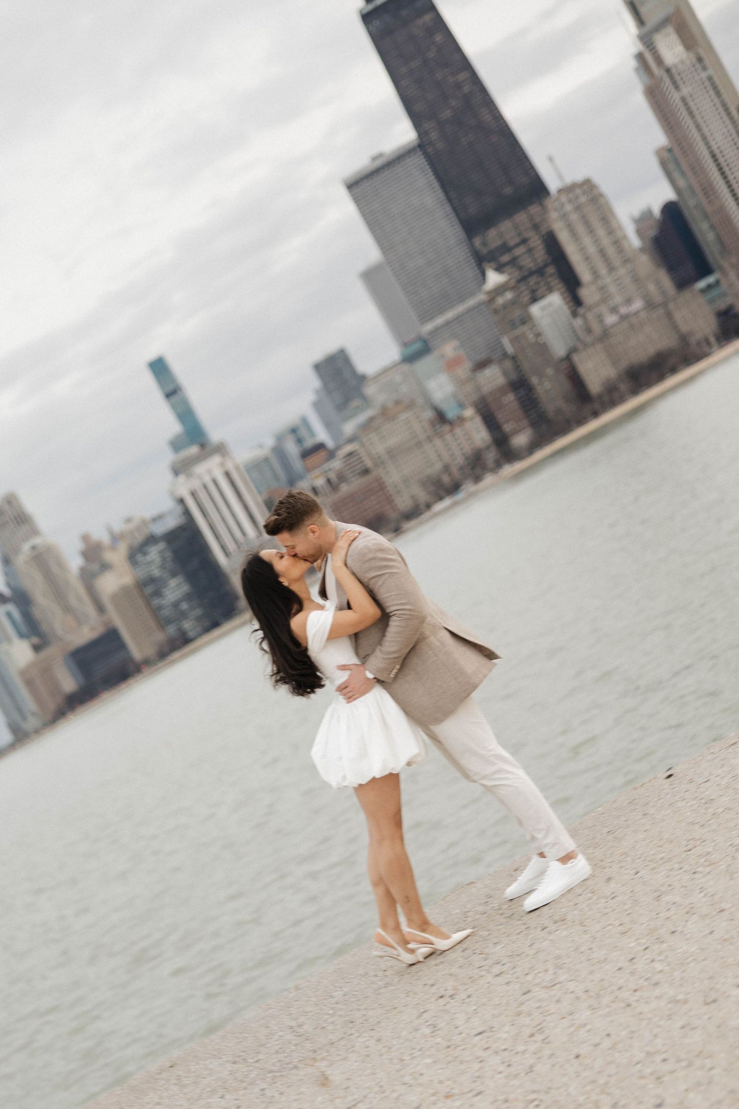 Couple sharing a romantic kiss by the Chicago lakefront with city skyline backdrop.