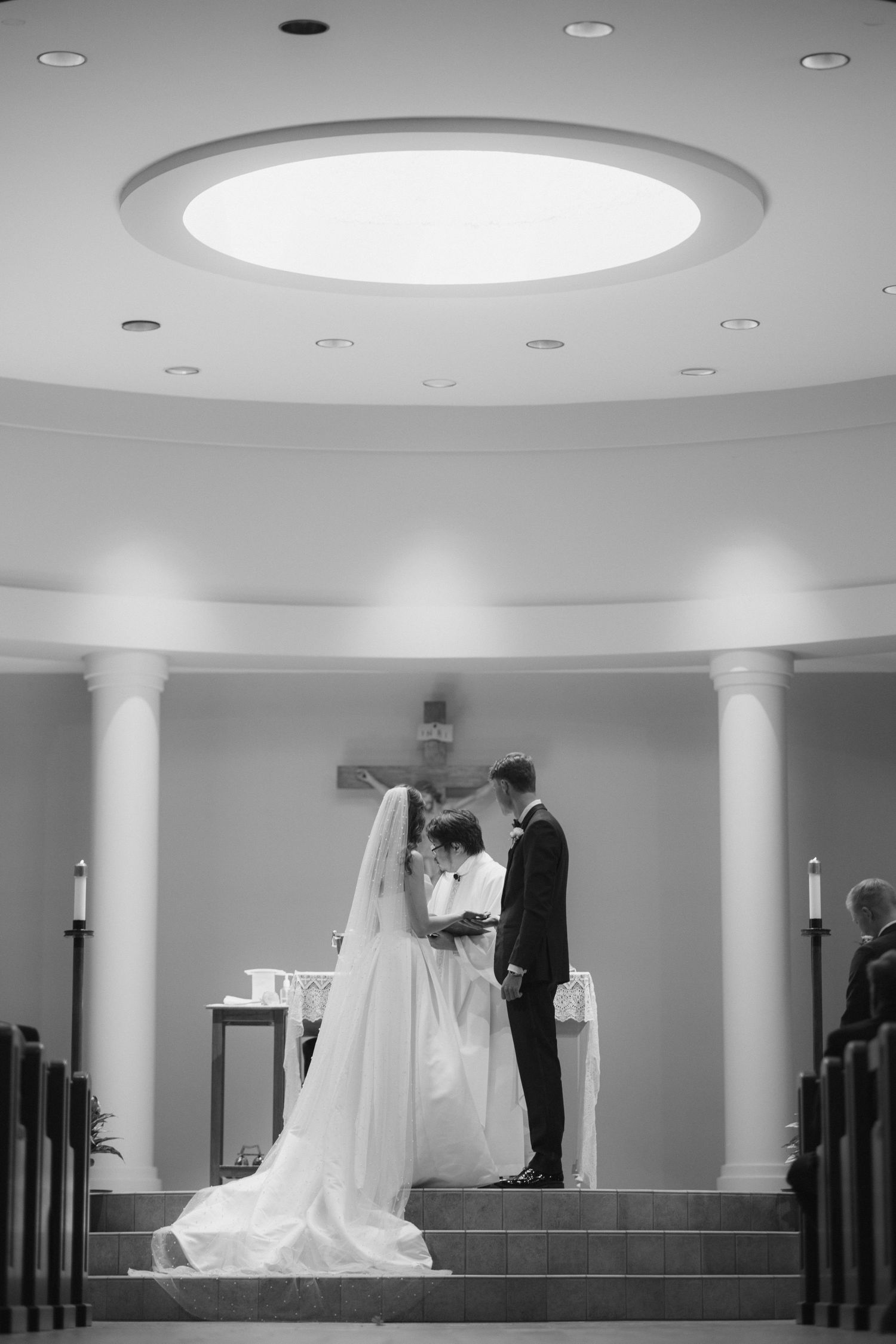 Black and white photo of a bride and groom exchanging vows at a church altar with columns and a crucifix.