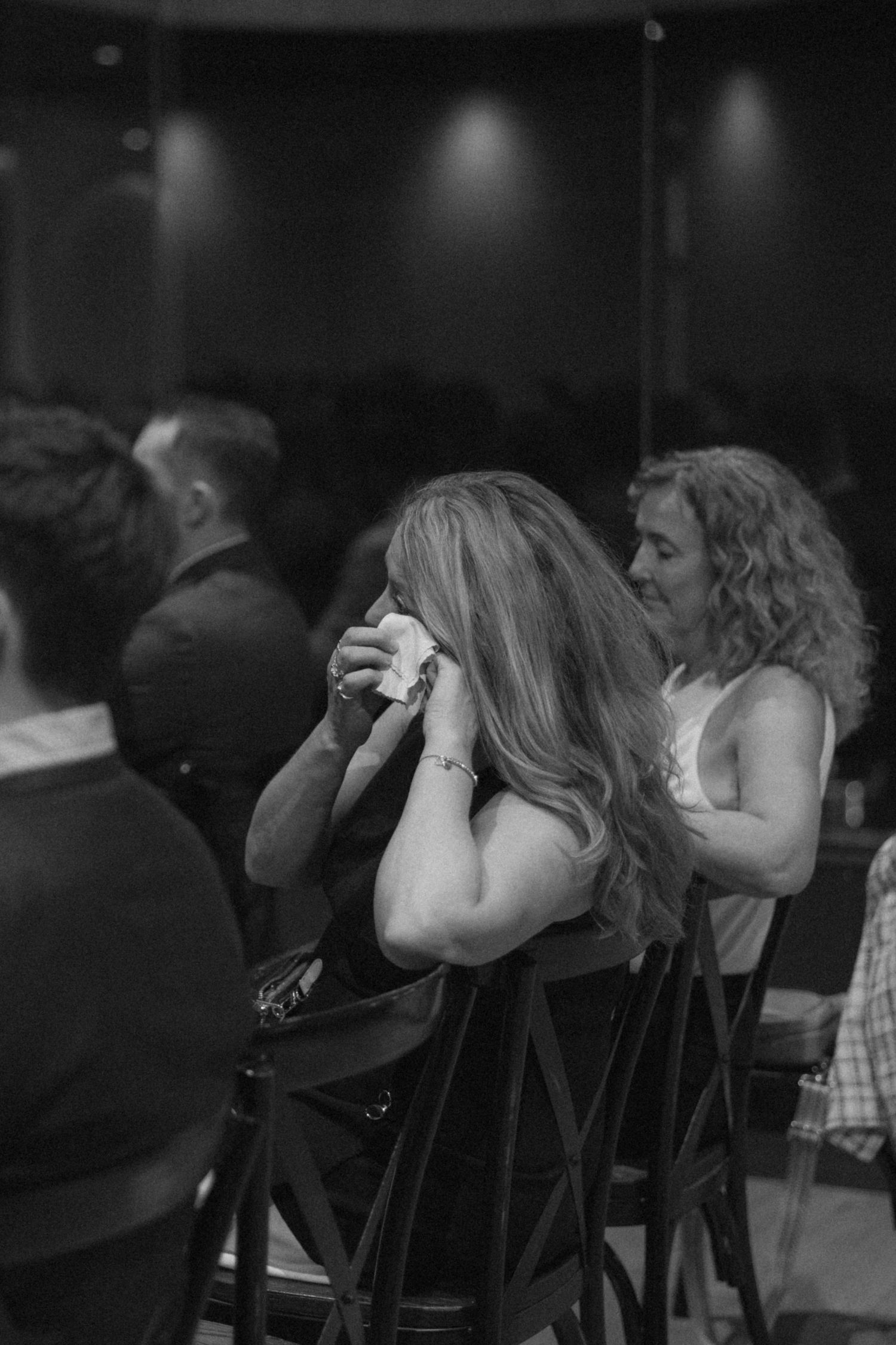 Emotional wedding guest wiping tears while seated at reception in black and white photo.