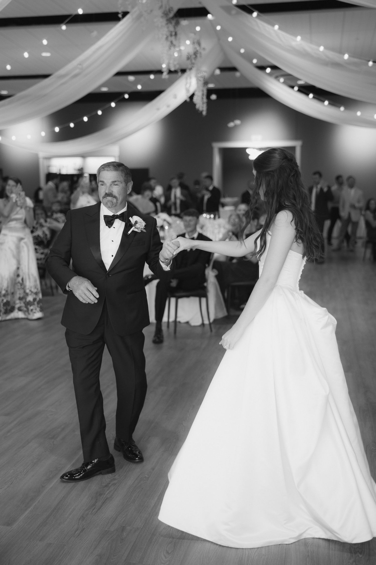 Black and white photo of a bride and her father sharing a touching father-daughter dance at an elegant wedding reception.