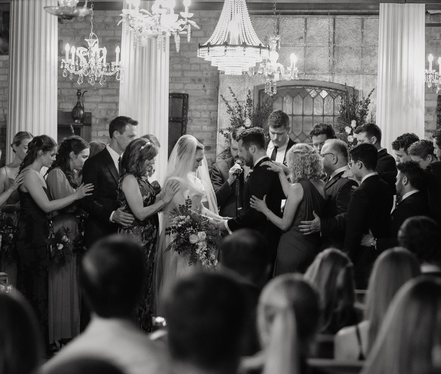 A black and white panoramic shot of guests dancing and mingling at an elegant reception with chandeliers overhead.