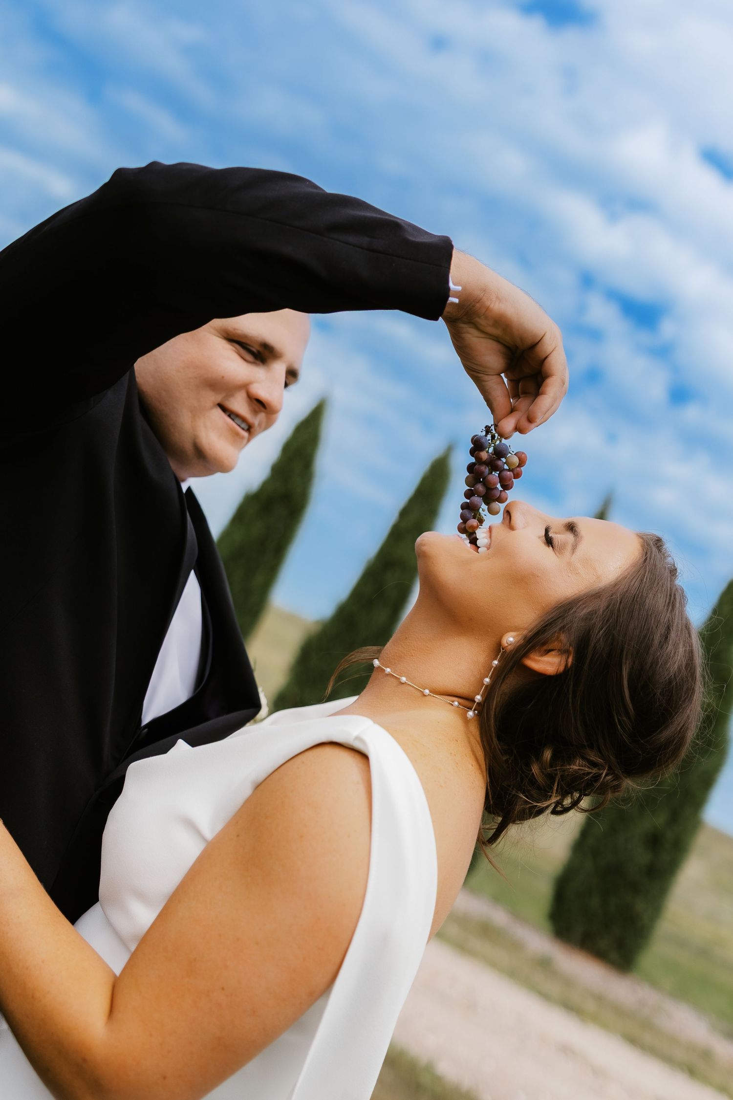 Artistic wedding photography captures romantic poses against blue sky and countryside backdrop.