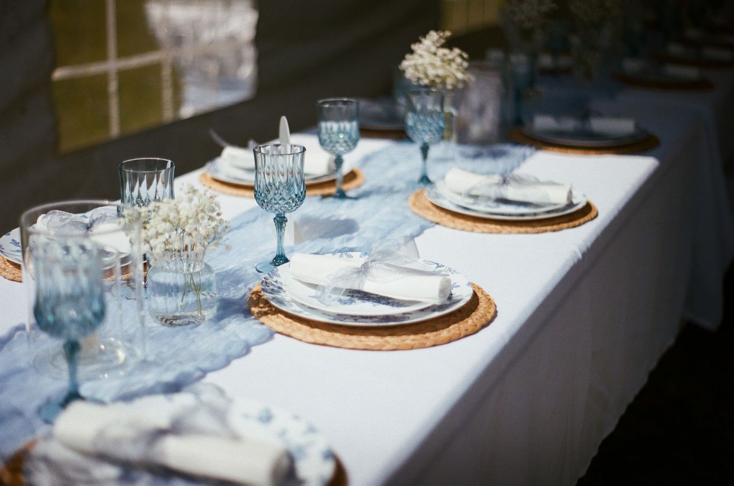 An elegant table setting with blue linens, copper chargers, and delicate white floral centerpieces extends down a long dining table.