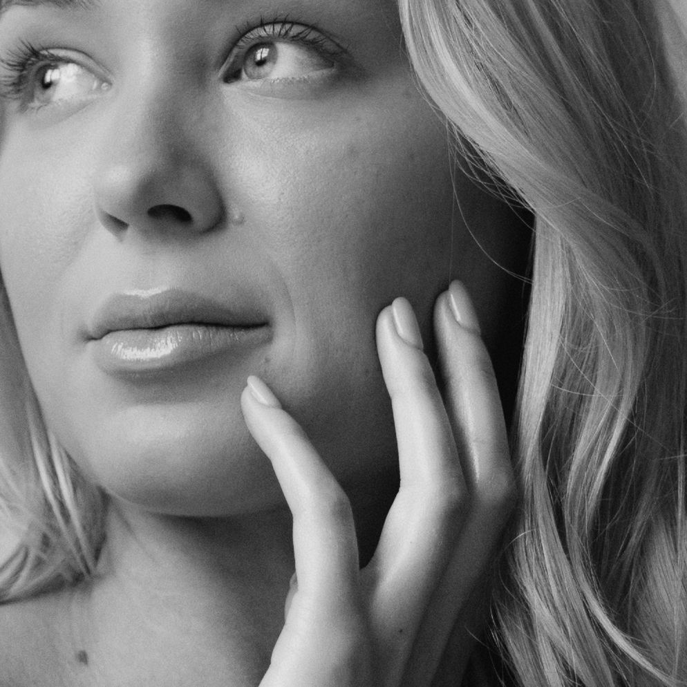 Black and white artistic portrait showing delicate hand gesture and soft profile lighting against dark background.