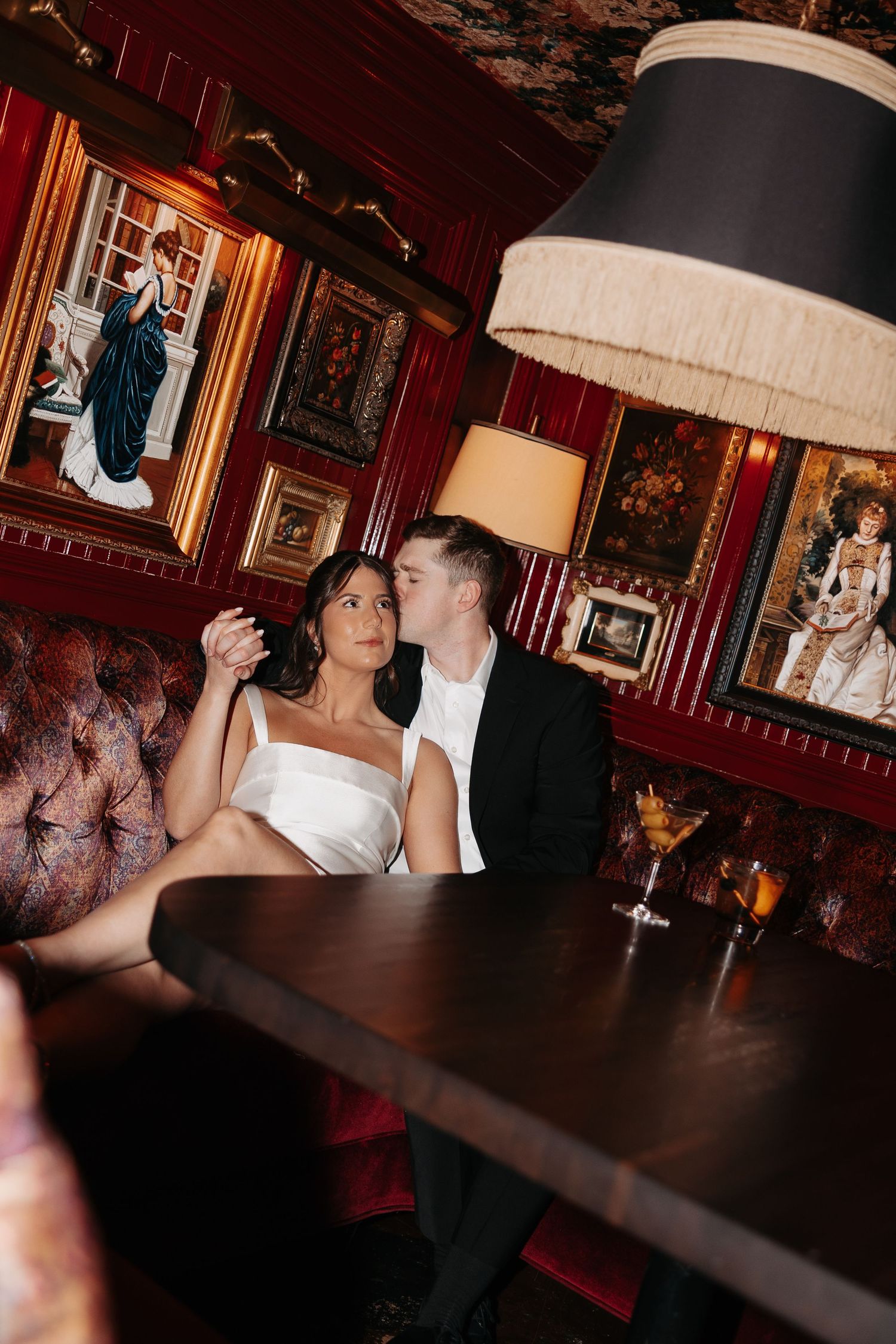 A couple shares an intimate moment in a dimly lit vintage bar with red walls and ornate decor.