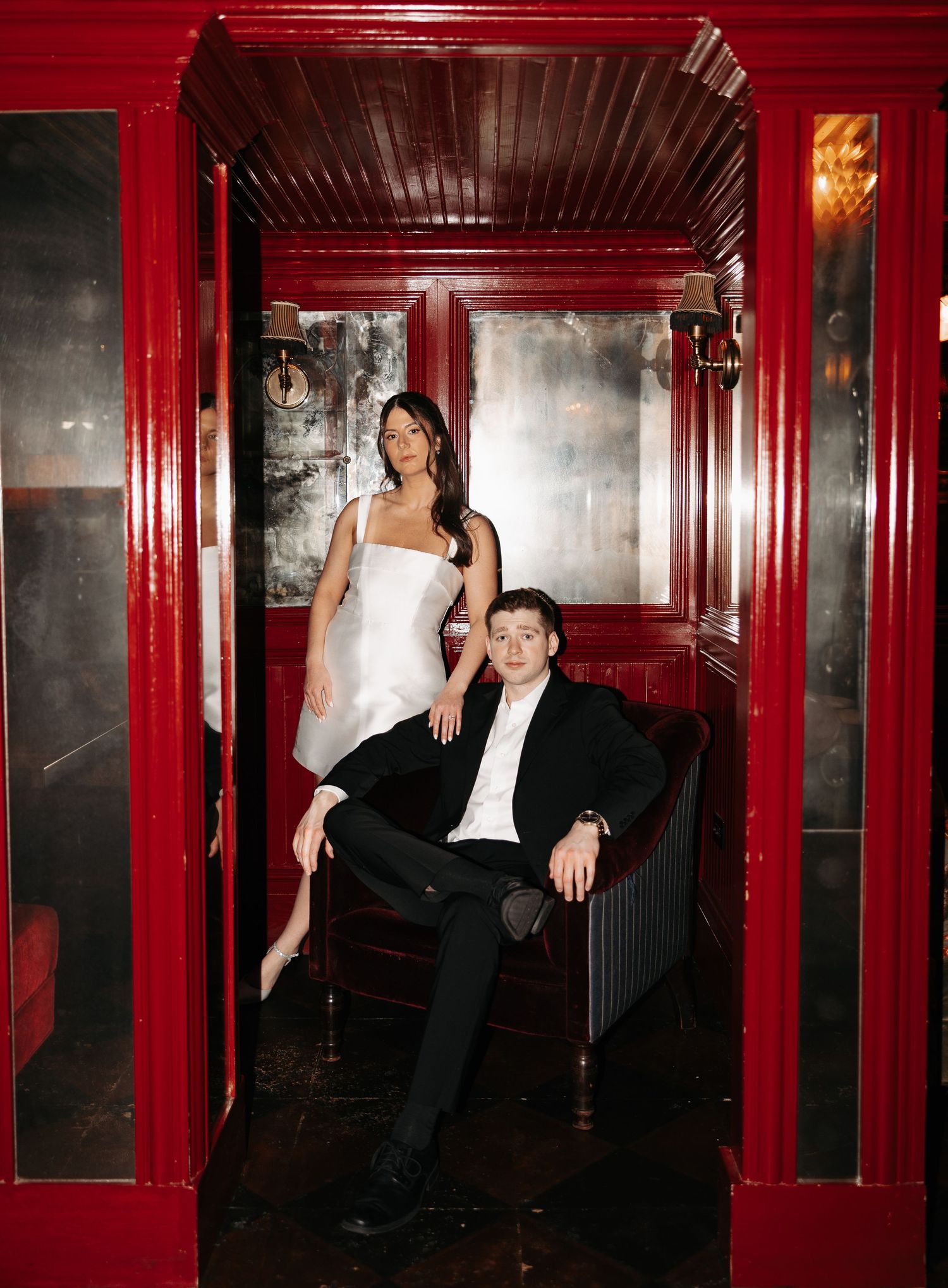 A couple poses in a dramatic red-walled hallway with vintage architectural details.