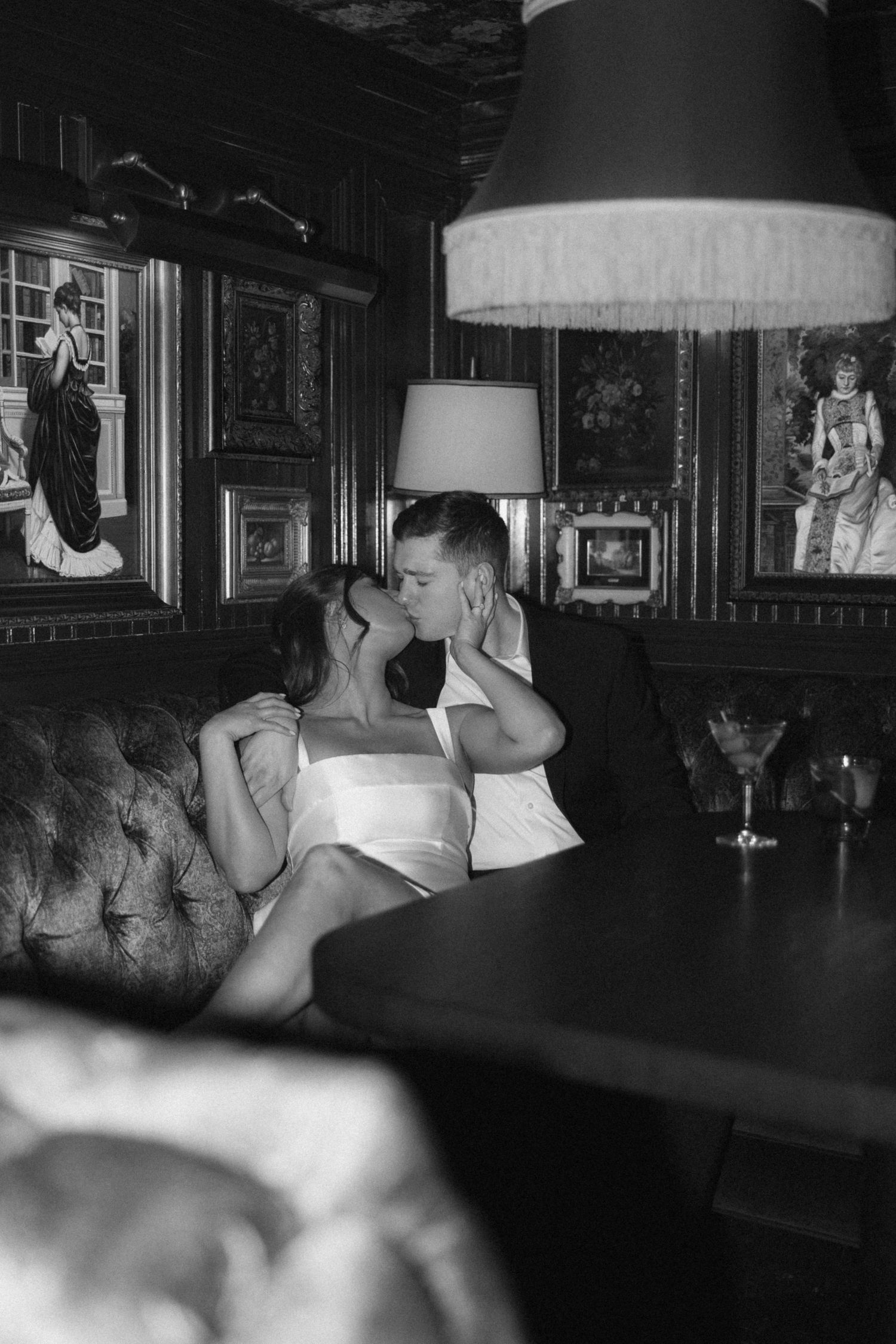 Black and white photograph of people seated at a dimly lit bar with framed artwork on the walls.