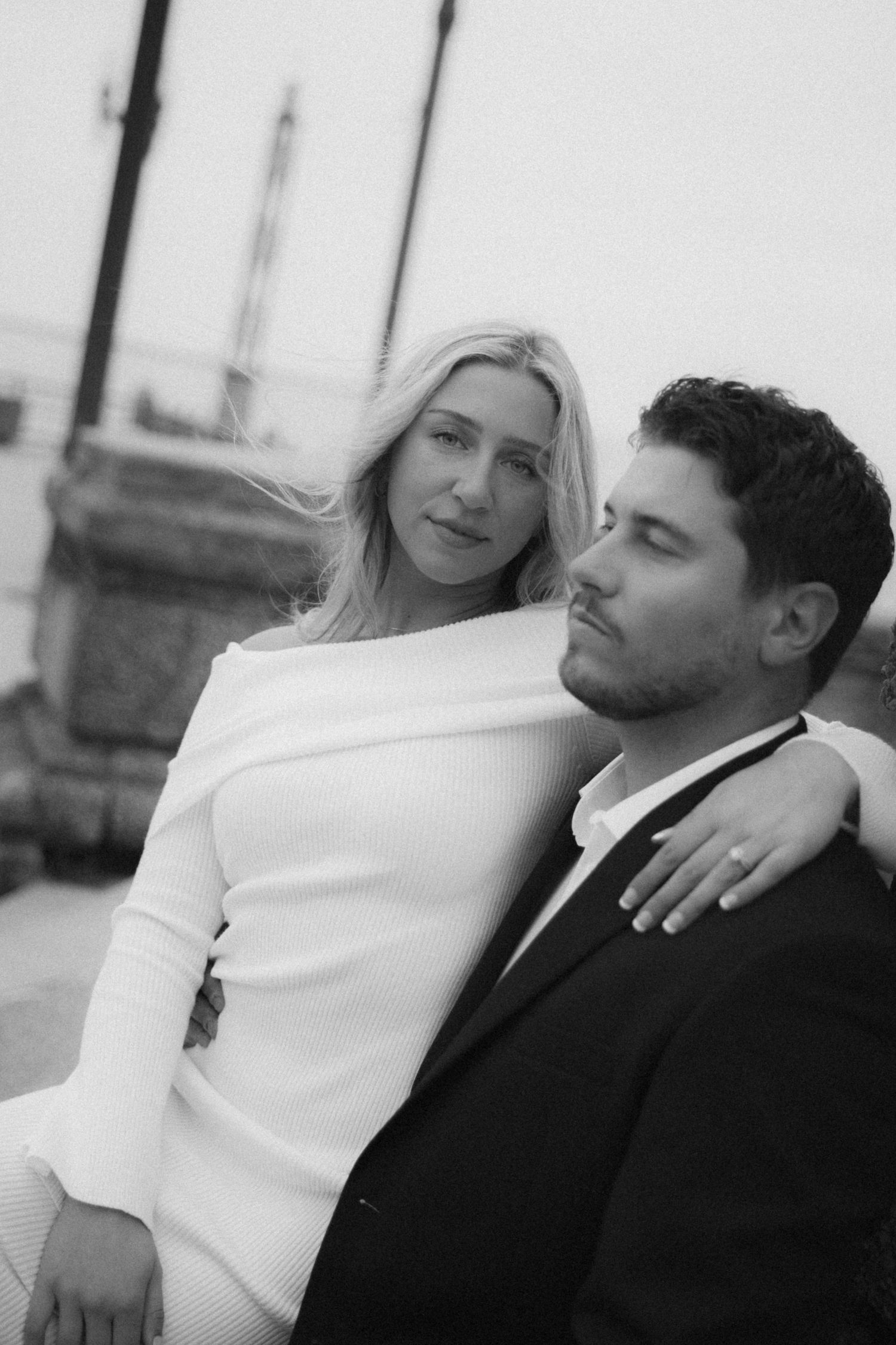Black and white romantic portrait of a couple embracing outdoors, with the person in white leaning against one in dark suit.