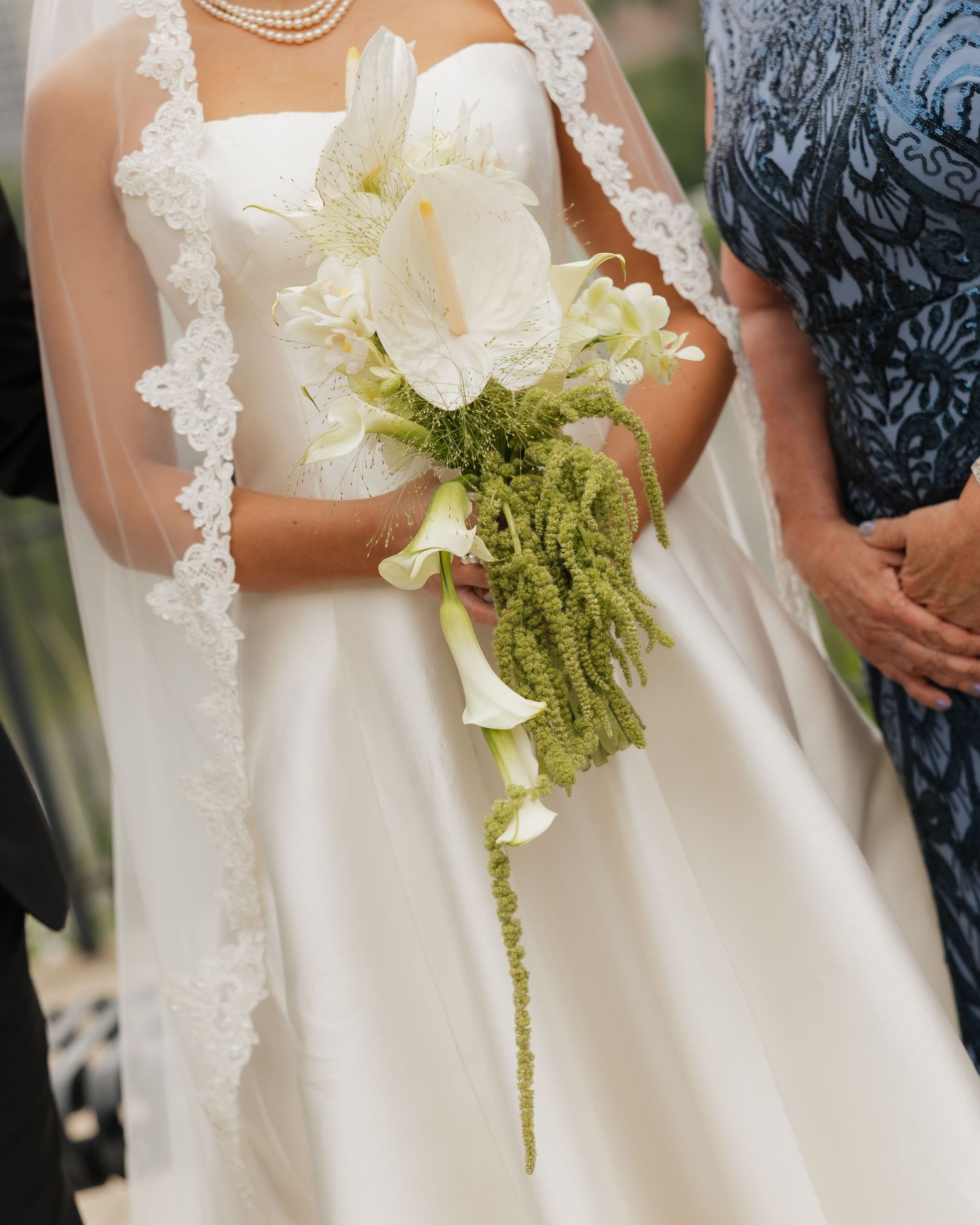 Bride in white strapless gown holding elegant cascading bouquet of white calla lilies and green amaranthus.