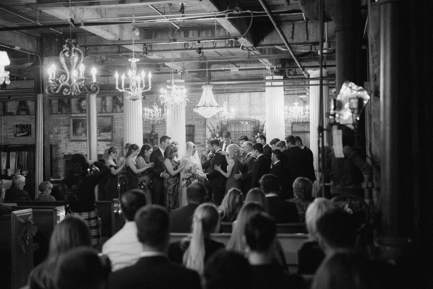 A black and white photograph shows a crowded indoor market with vendors and shoppers under industrial lighting.
