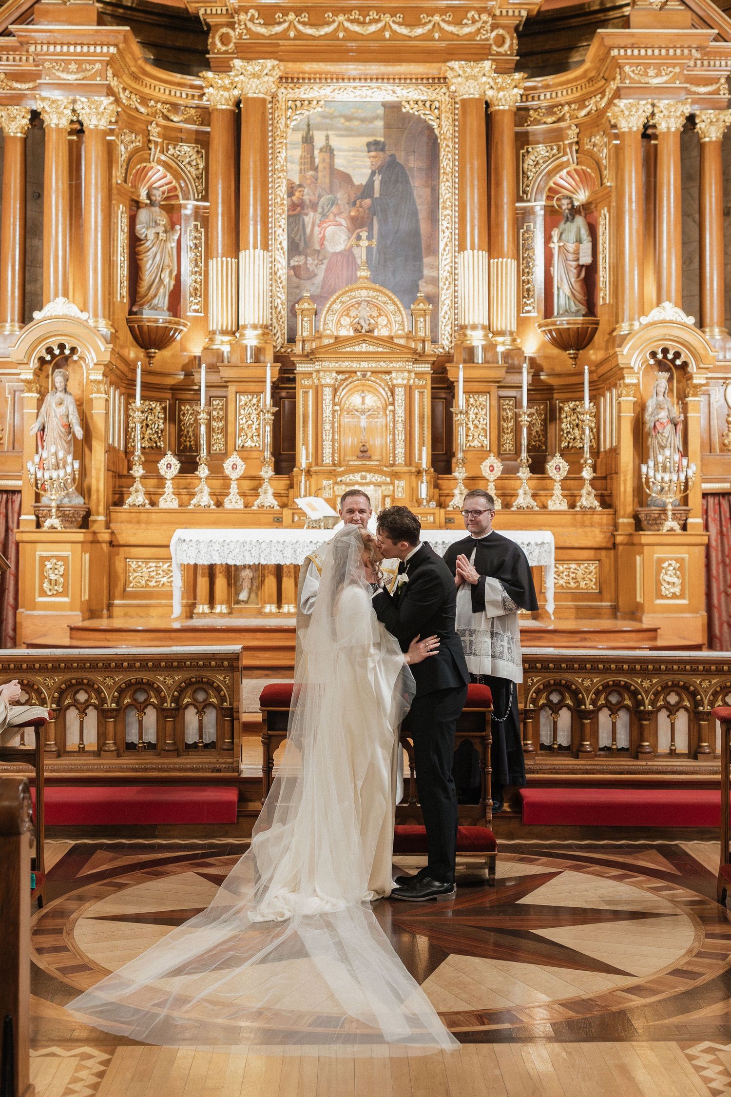 A wedding ceremony takes place in an ornate church with golden altar and decorative architecture.