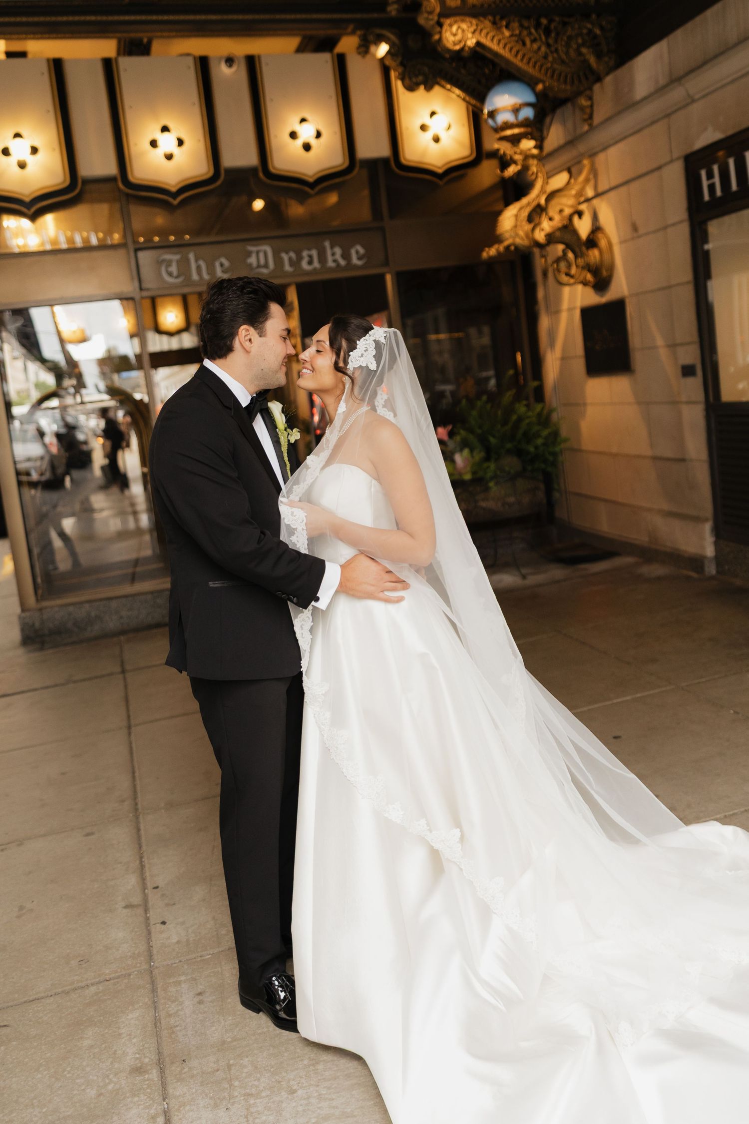 Bride and groom share a romantic kiss outside The Drake Hotel, bride in a flowing white gown with long veil.