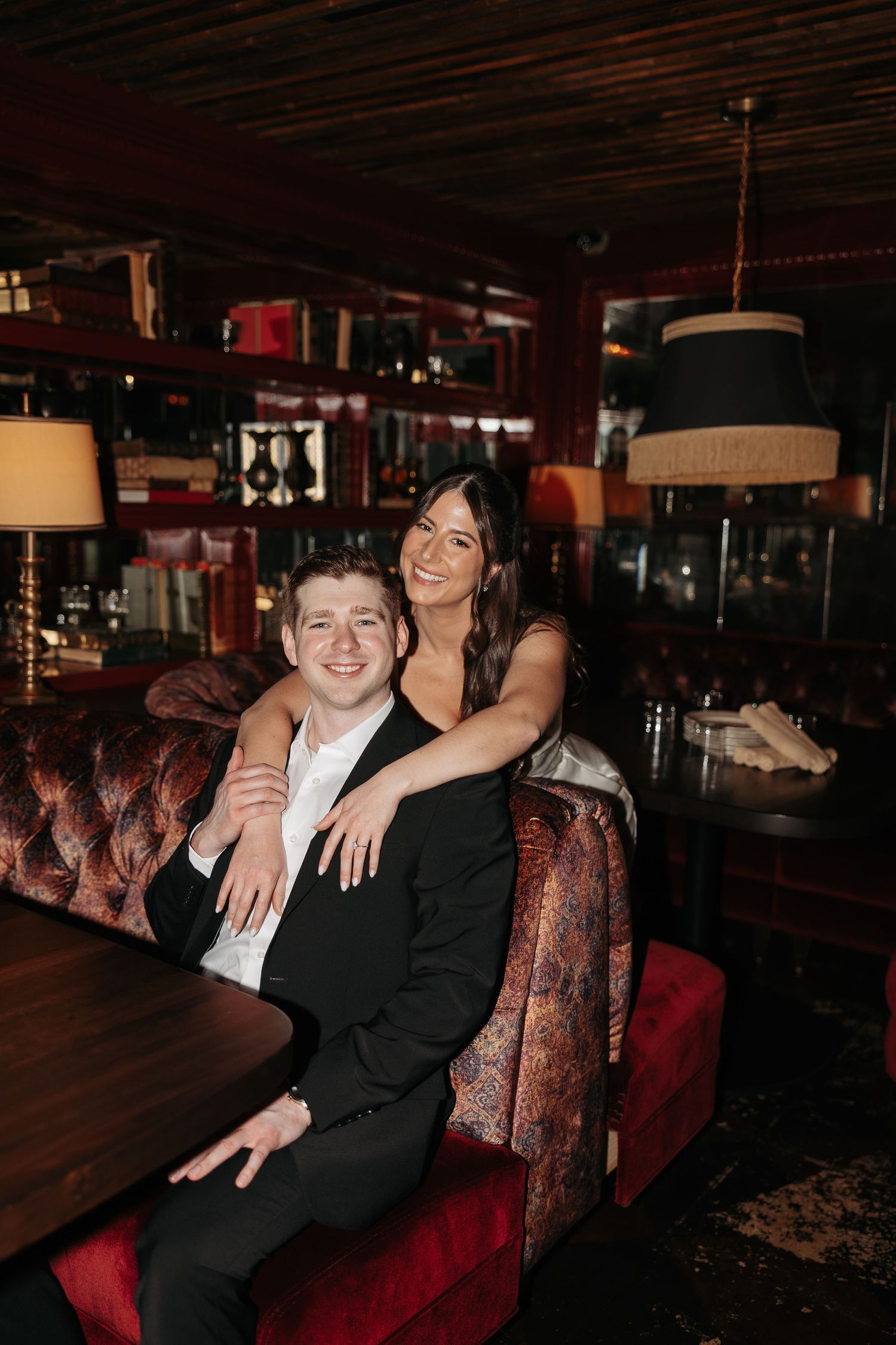 Couple lounging on red velvet seating in a cozy restaurant or bar setting.
