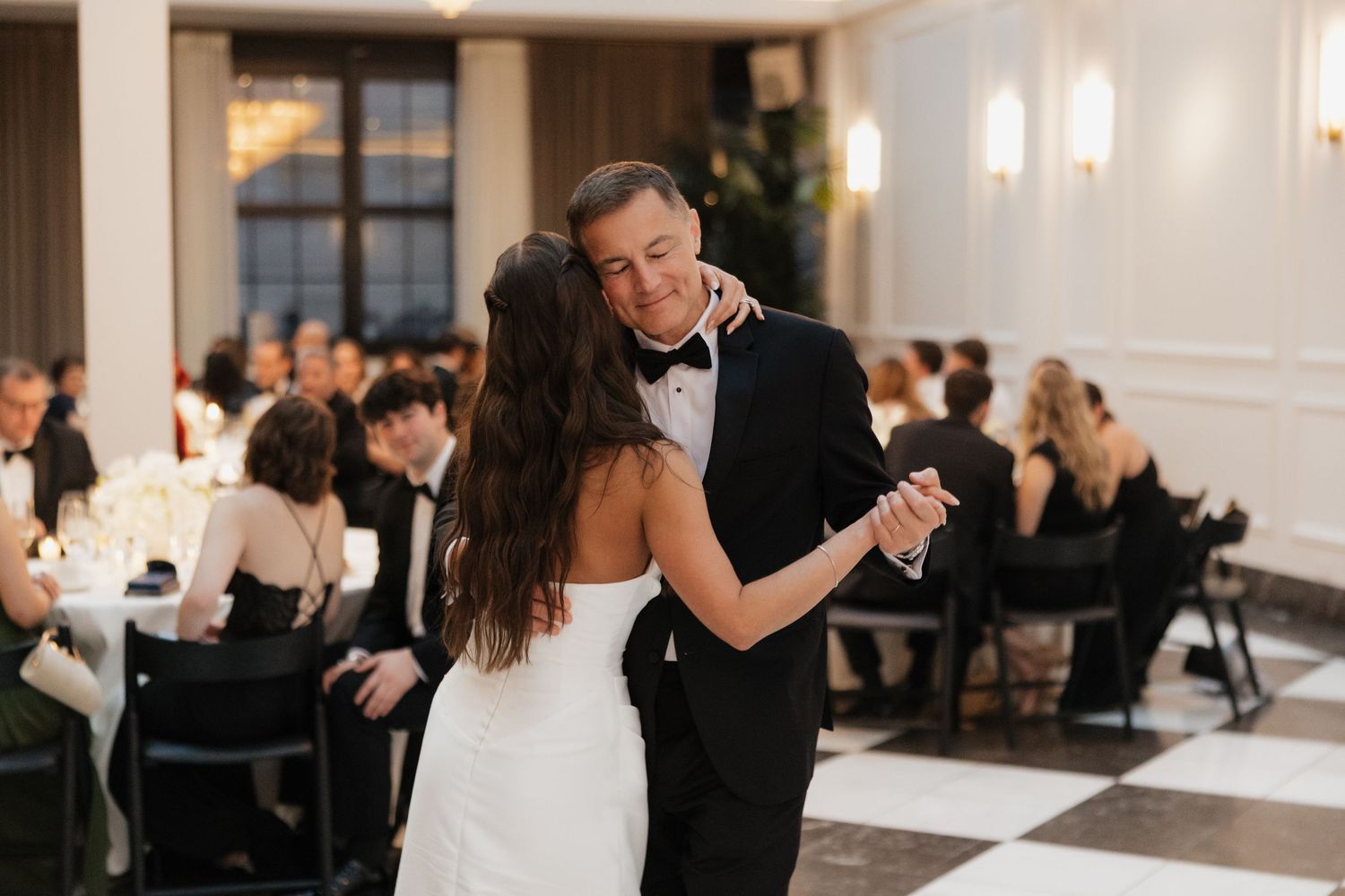 Bride and groom share their first dance in an elegant ballroom with black and white checkered floors.