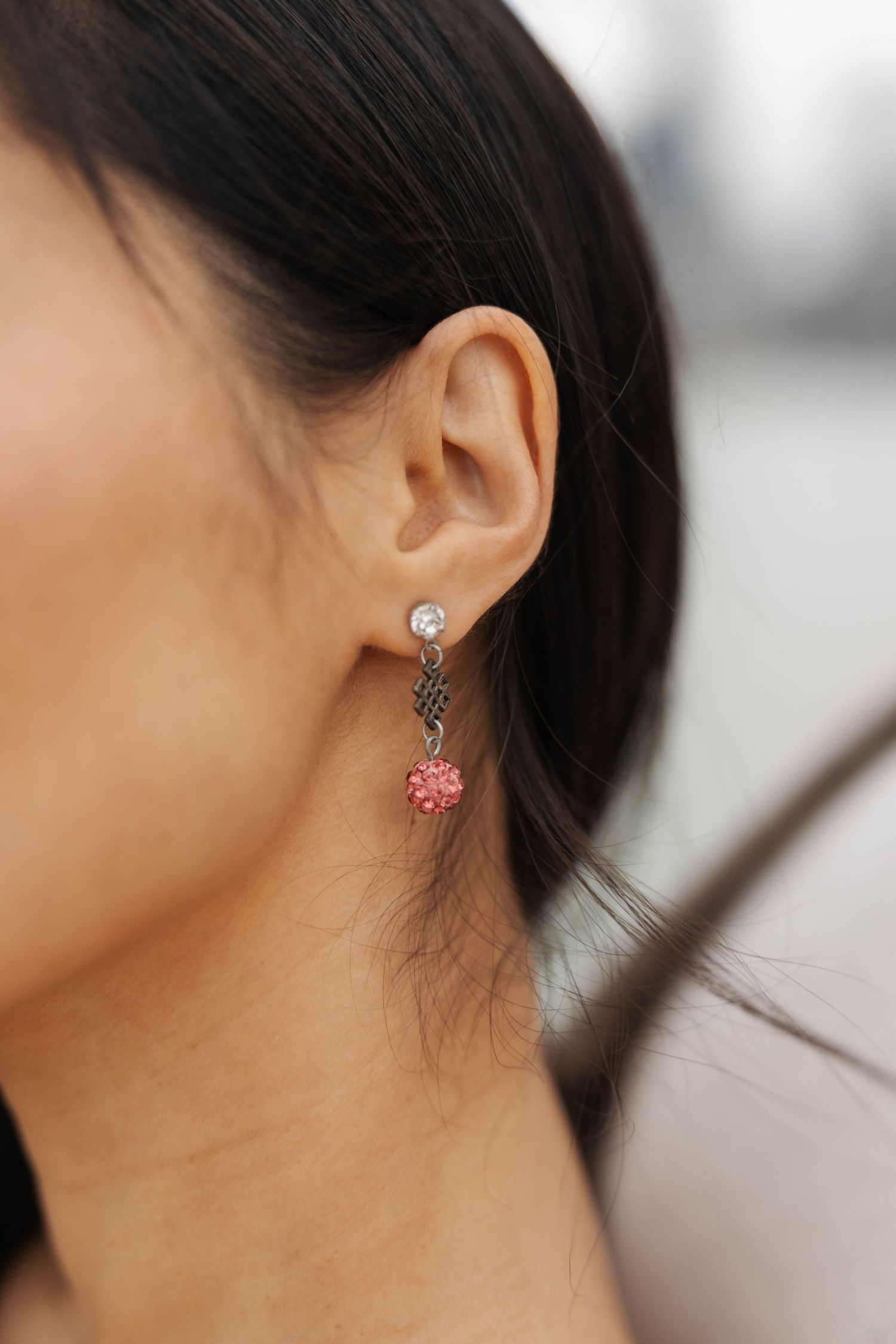 Close-up of dangle earring featuring clear crystal stud, gunmetal chain, and pink rhinestone flower charm.