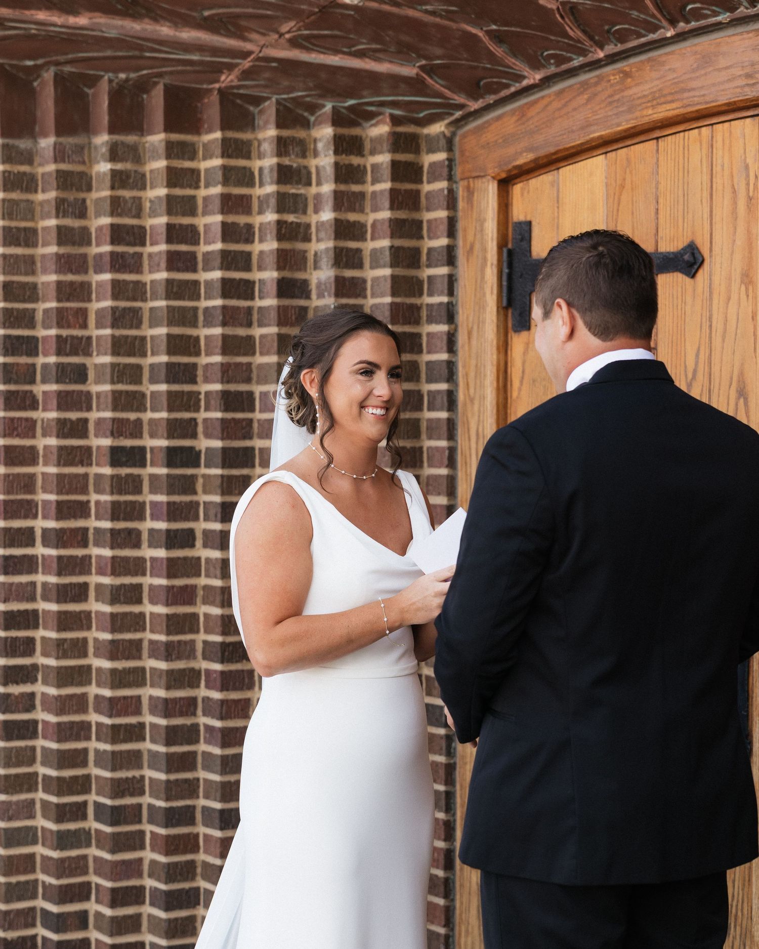 Intimate wedding moment unfolds against textured brick wall and wooden door.