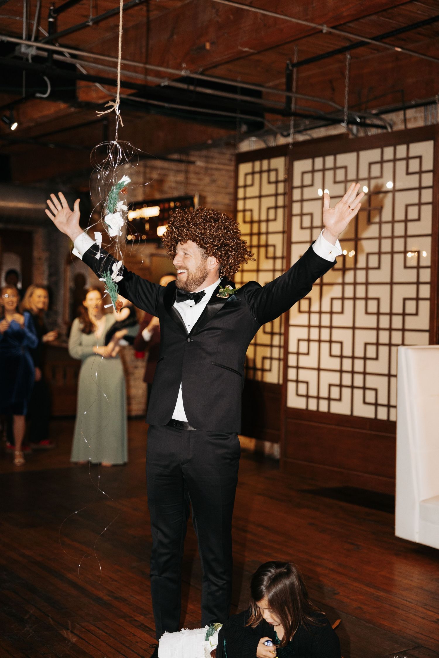 A joyful celebration on a rustic dance floor with exposed brick walls and geometric wall panels at a wedding reception.