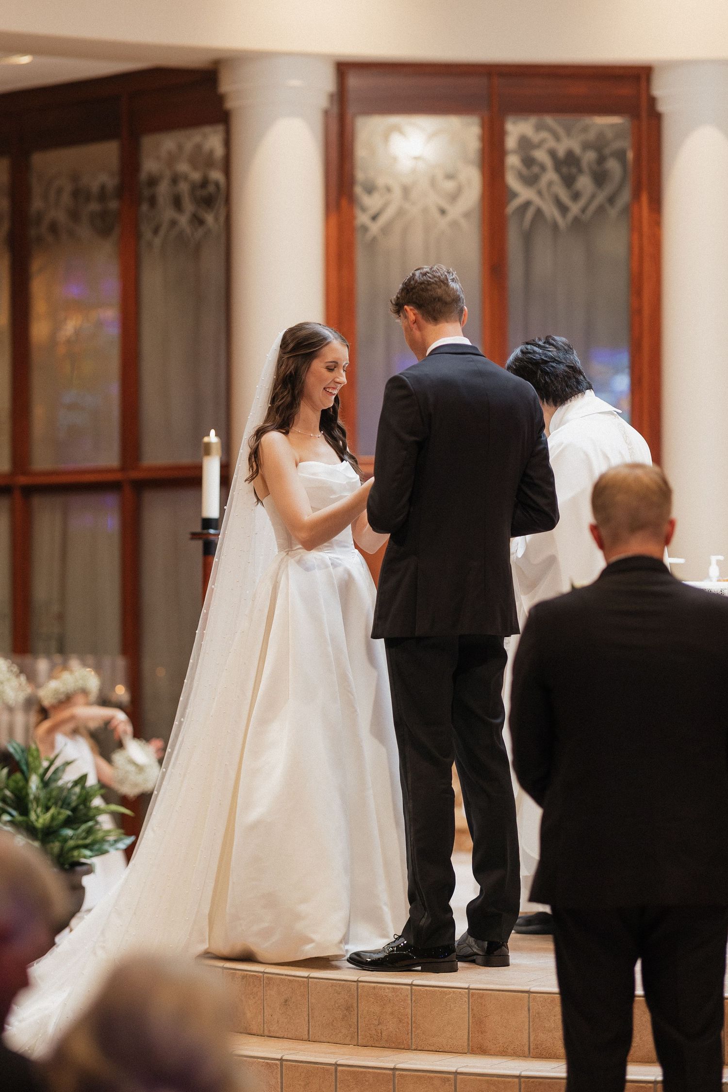 Bride and groom exchanging vows at elegant wedding ceremony altar with candles and stained glass windows.