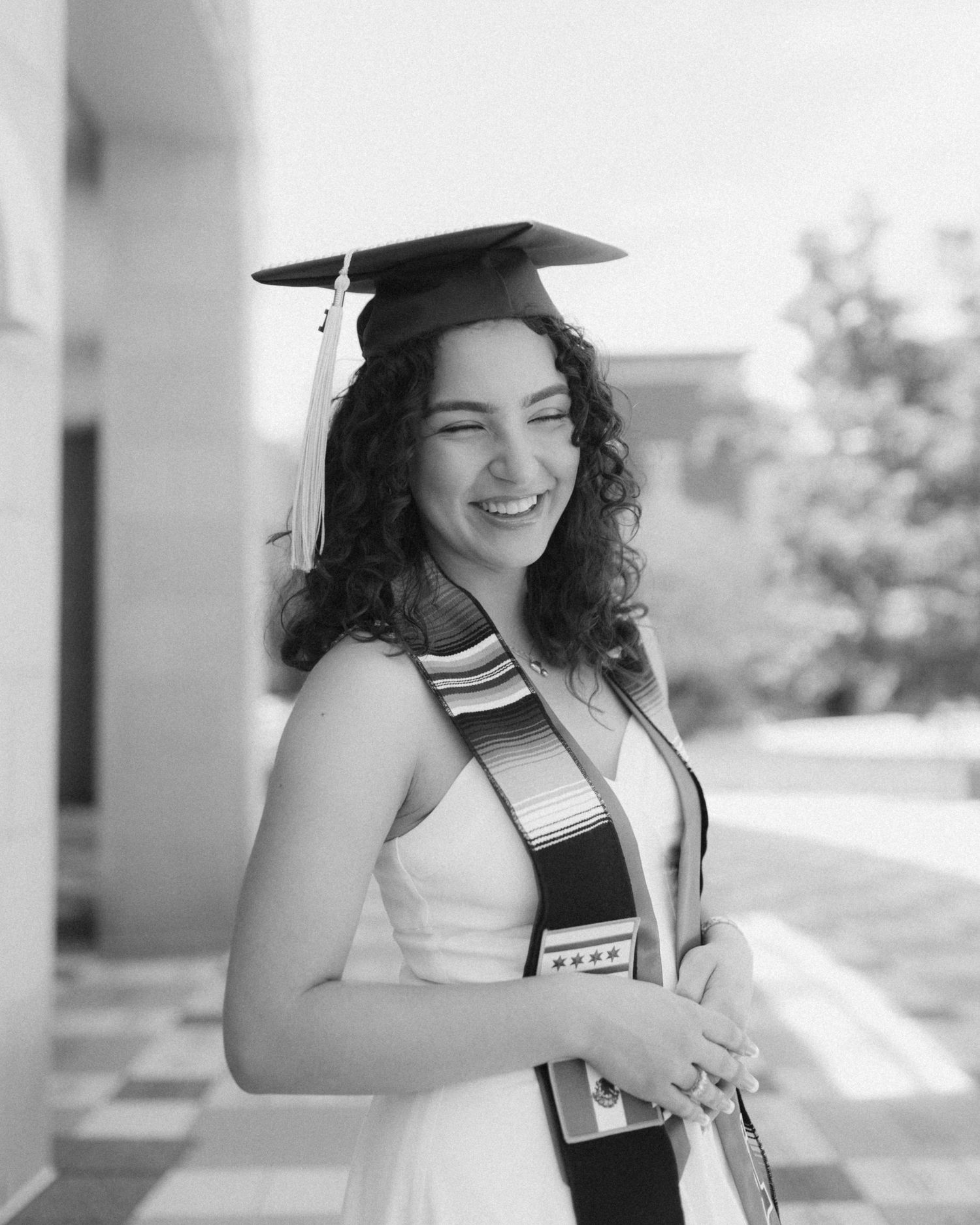 A graduate in cap and gown smiles joyfully while celebrating their academic achievement in black and white photography.