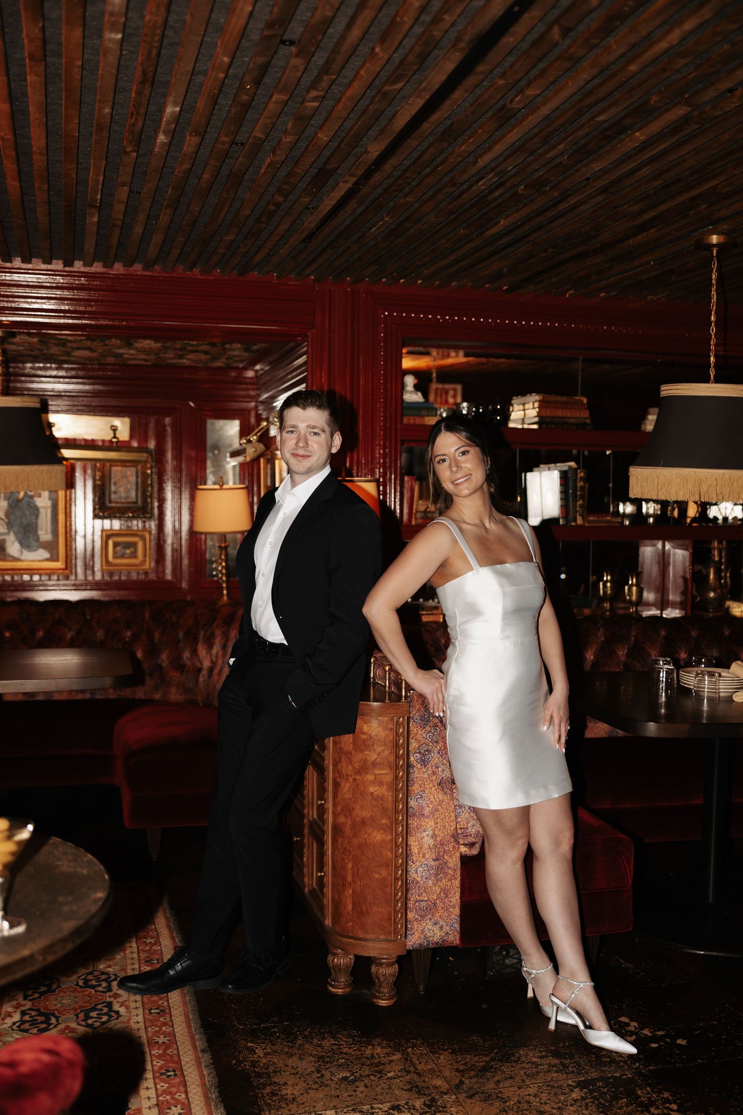 A couple dancing in a dimly lit room with rustic wooden decor and red accents.