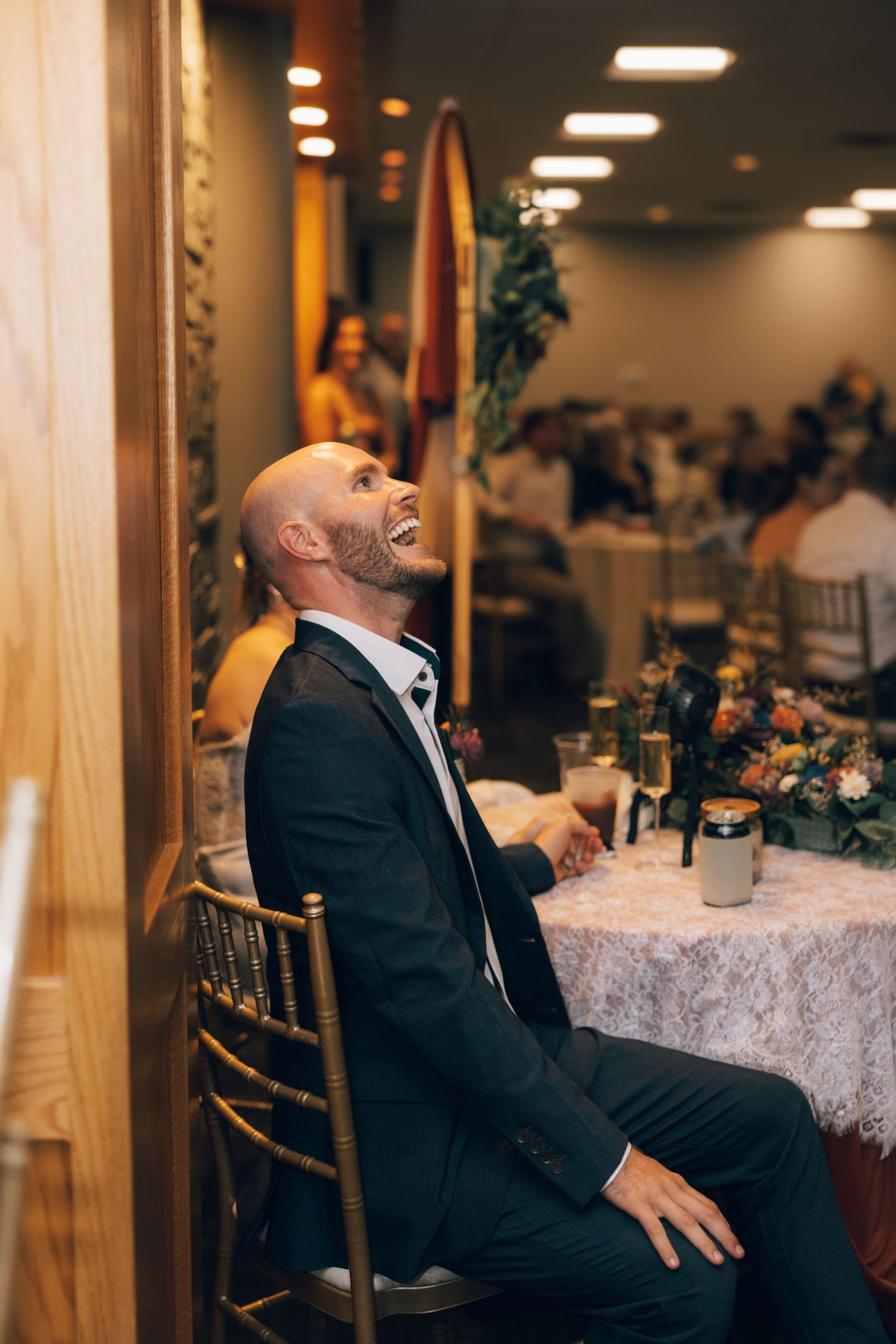 Person in formal attire reacting emotionally while seated at an indoor reception venue.
