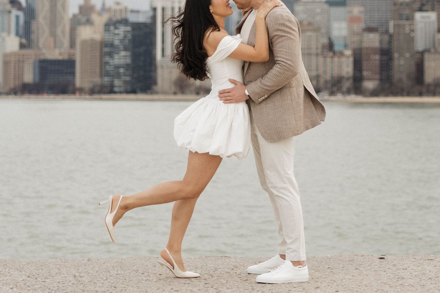 Close-up of couple embracing and kissing near waterfront with urban skyline in background.