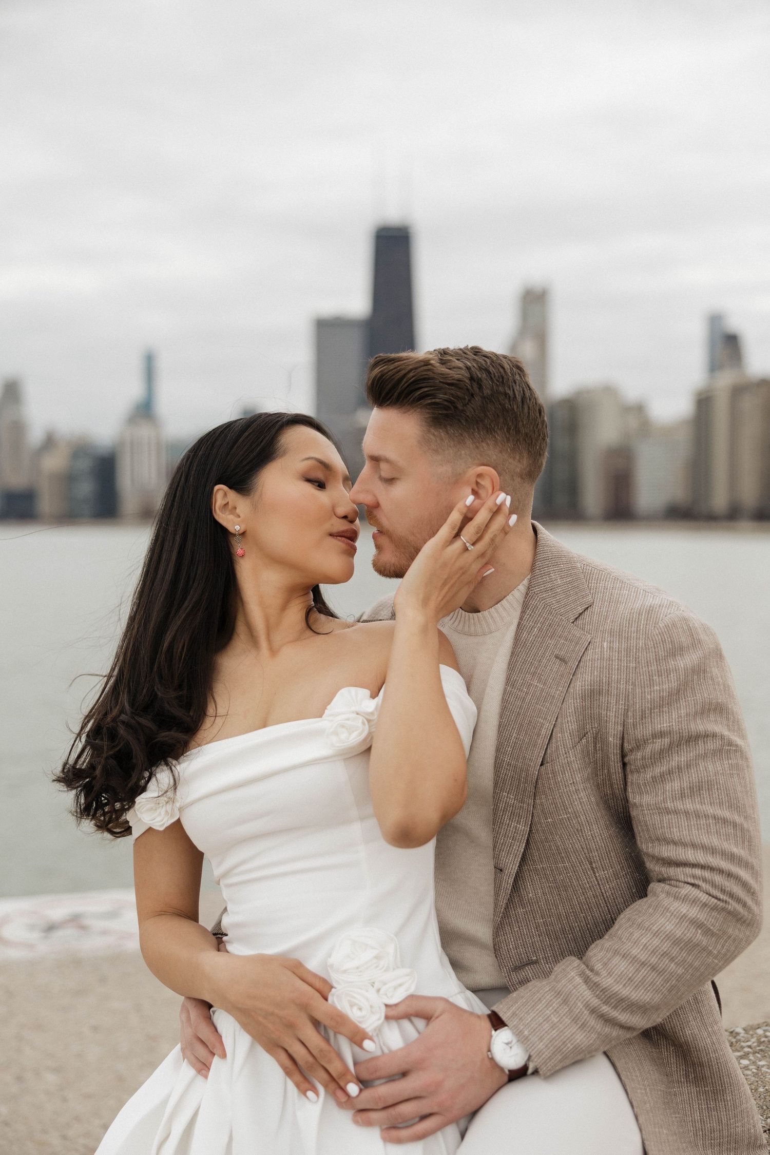 Couple sharing a romantic kiss in wedding attire with Chicago skyline backdrop near Lake Michigan.