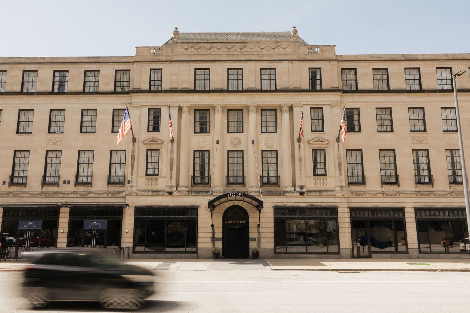 Historic beige stone building with American flags, large windows, and a grand entrance on a city street.