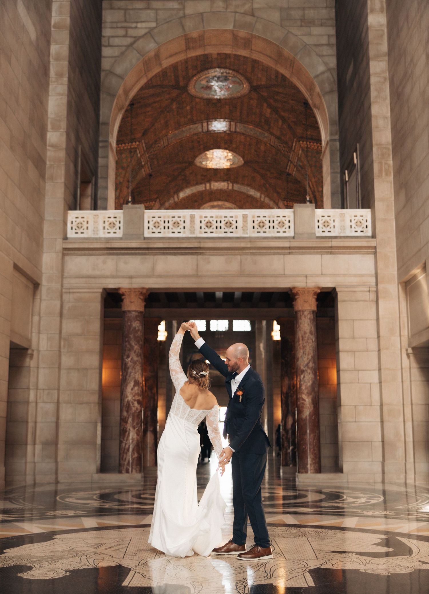 Wedding couple dancing in grand marble hallway with arched ceilings.