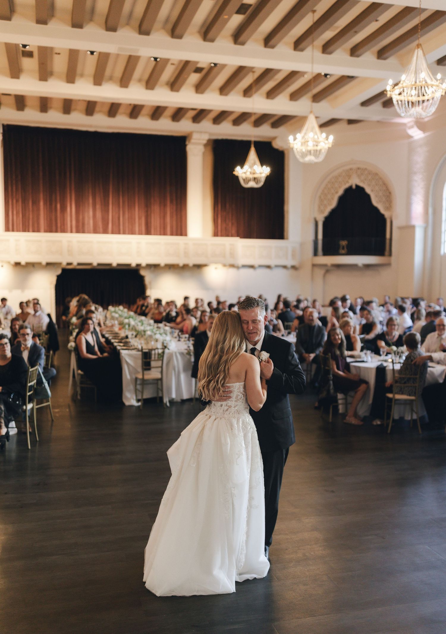Wedding reception in an elegant ballroom with crystal chandeliers and wooden beam ceiling.