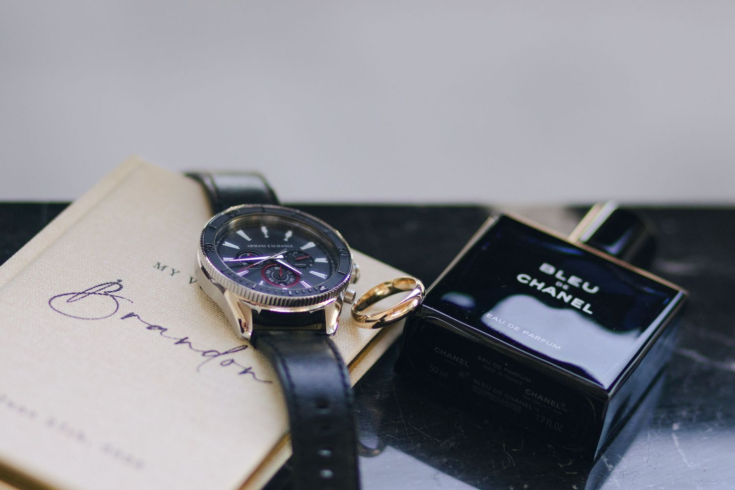 A luxury watch with a blue dial and gold accents sits elegantly on a black leather surface next to a book.