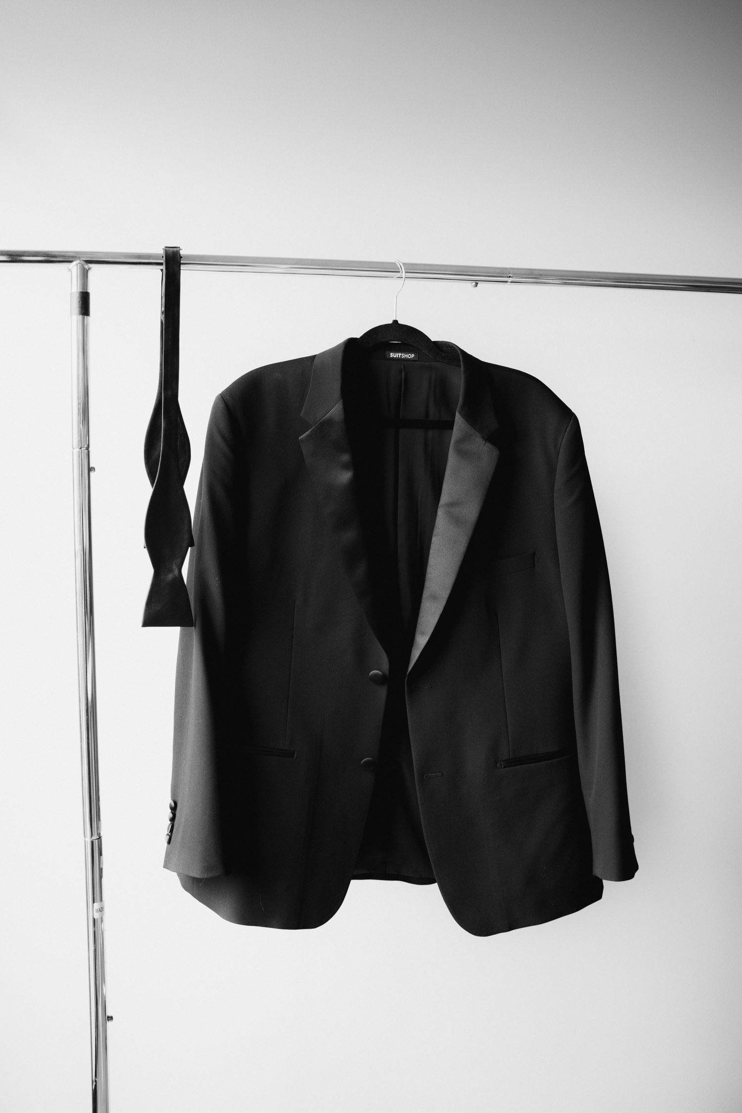 Black tuxedo jacket with satin lapels and bow tie hanging on a clothing rack, perfect for formal events.