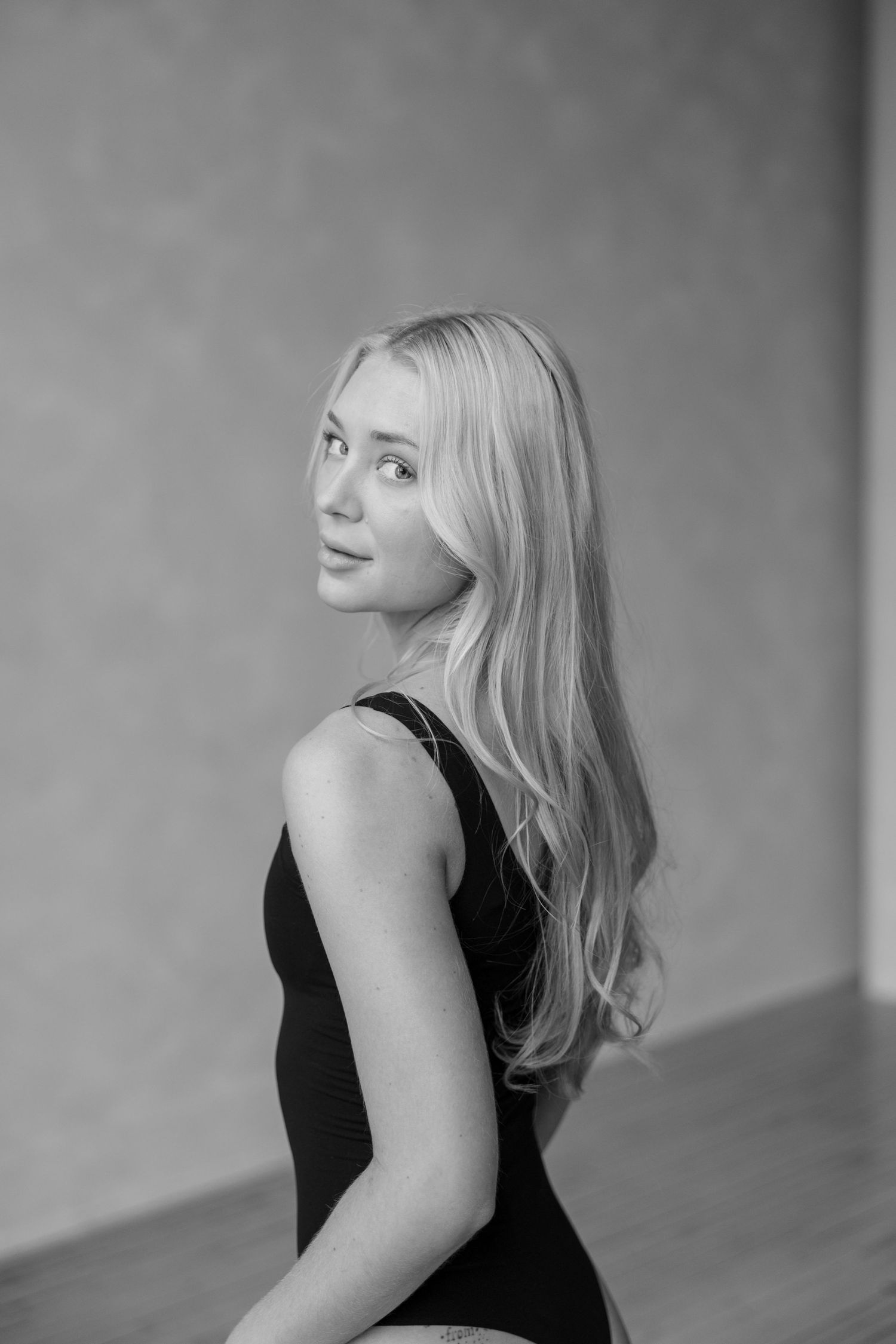 Black and white portrait of a woman with long blonde hair in a sleeveless black top looking over her shoulder.