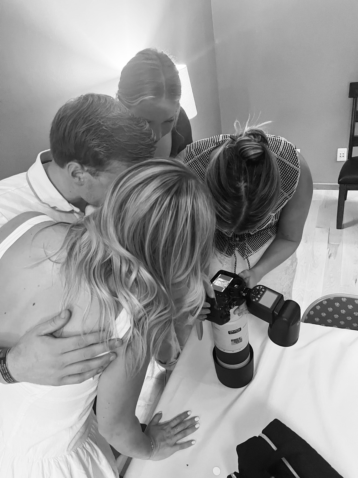 Black and white photo of people gathered around looking at a camera display during a photography session.