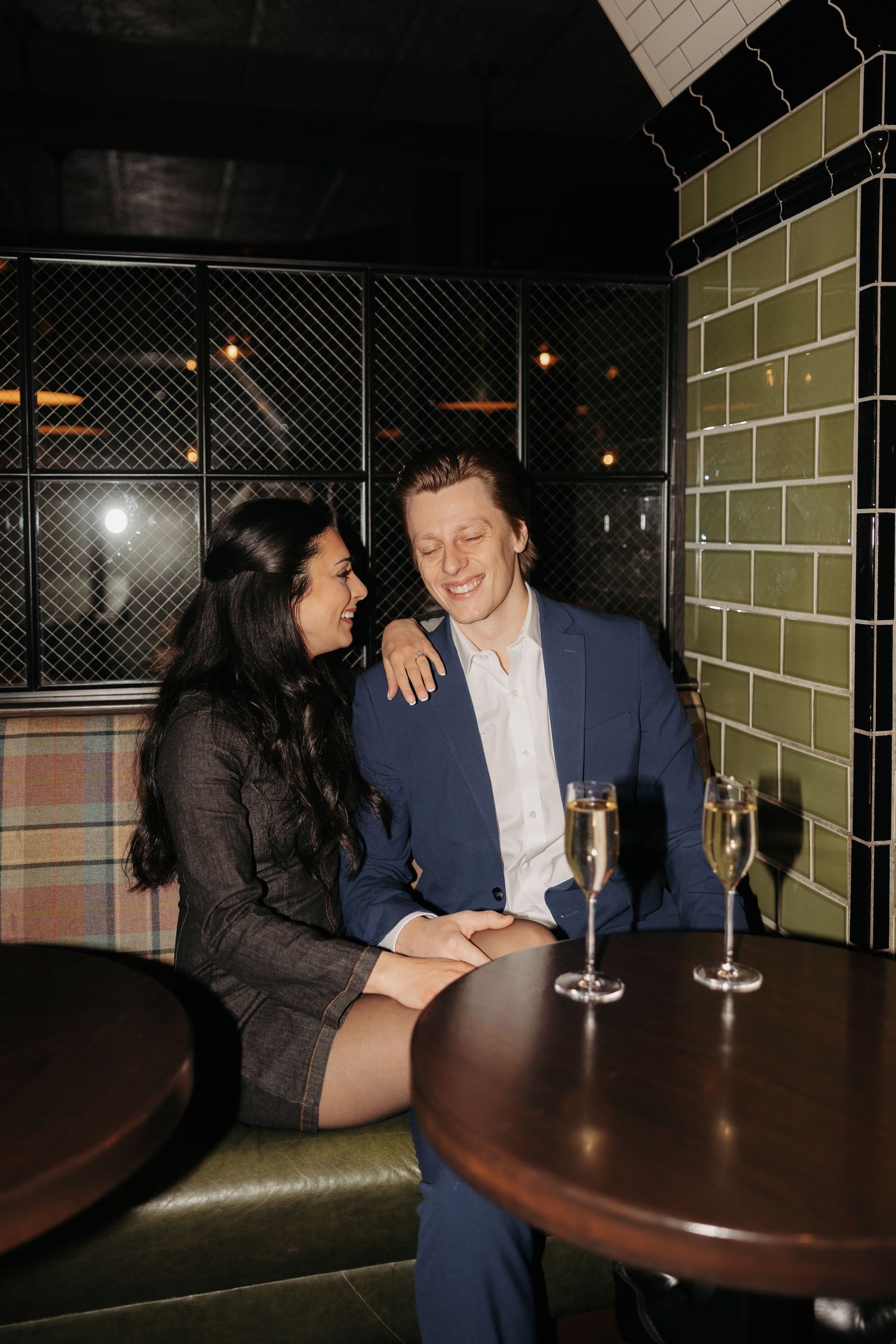 A couple shares an intimate moment at a dark wooden table in a bar setting.