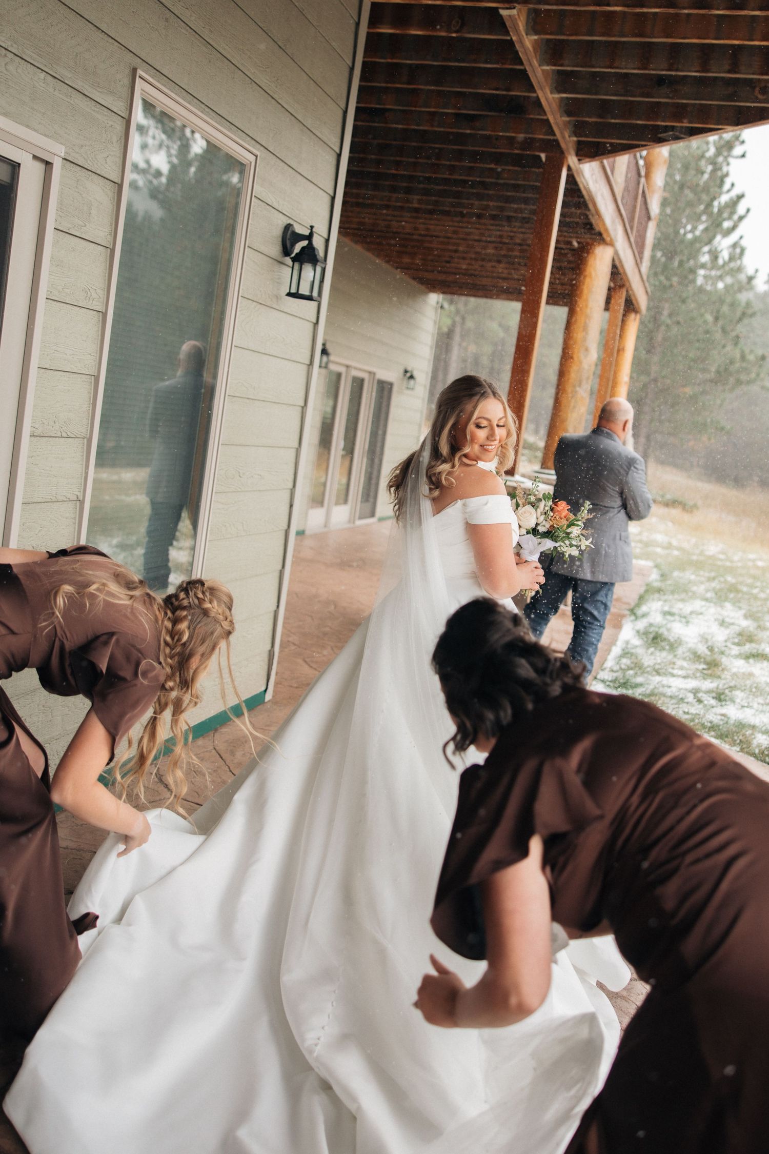 Wedding dress being bustled by attendants on a covered porch.