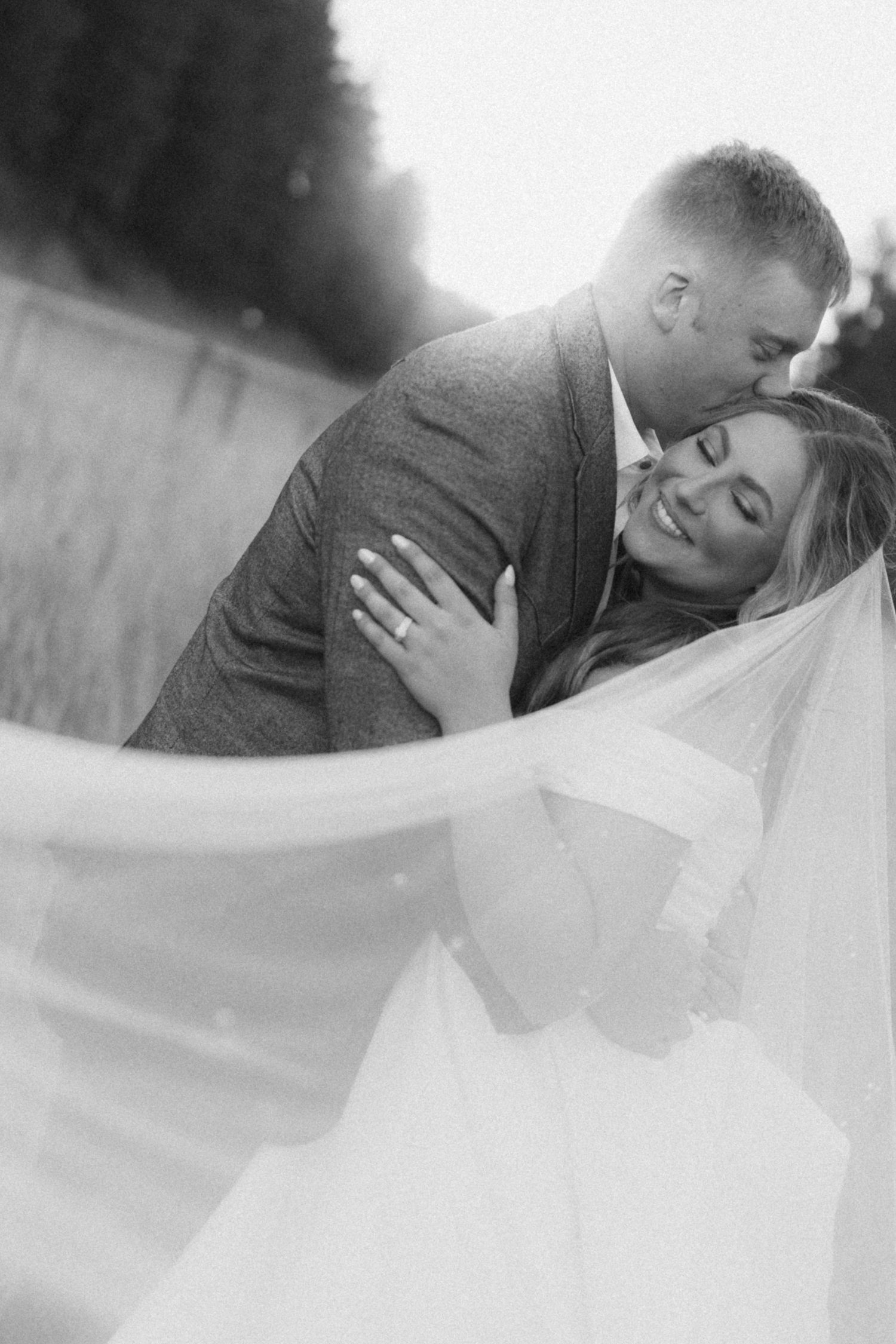 Romantic black and white photo with flowing wedding veil in outdoor setting.