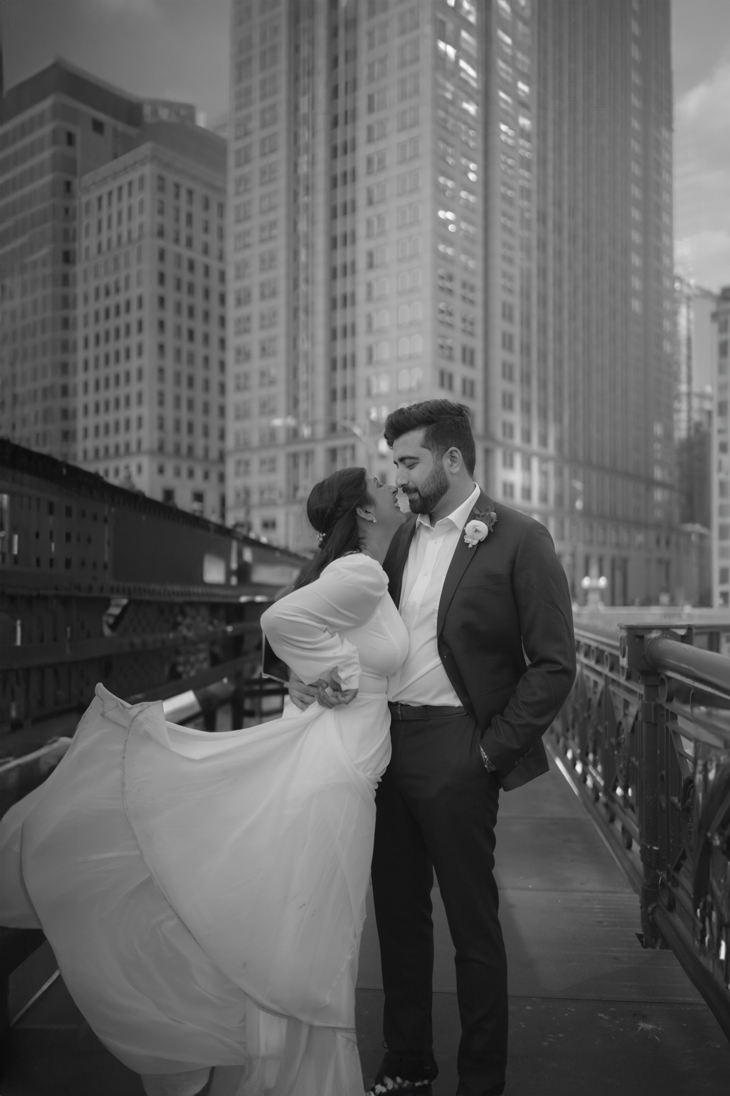 A romantic black and white wedding photo of a couple embracing on a bridge with Chicago skyscrapers in the background.