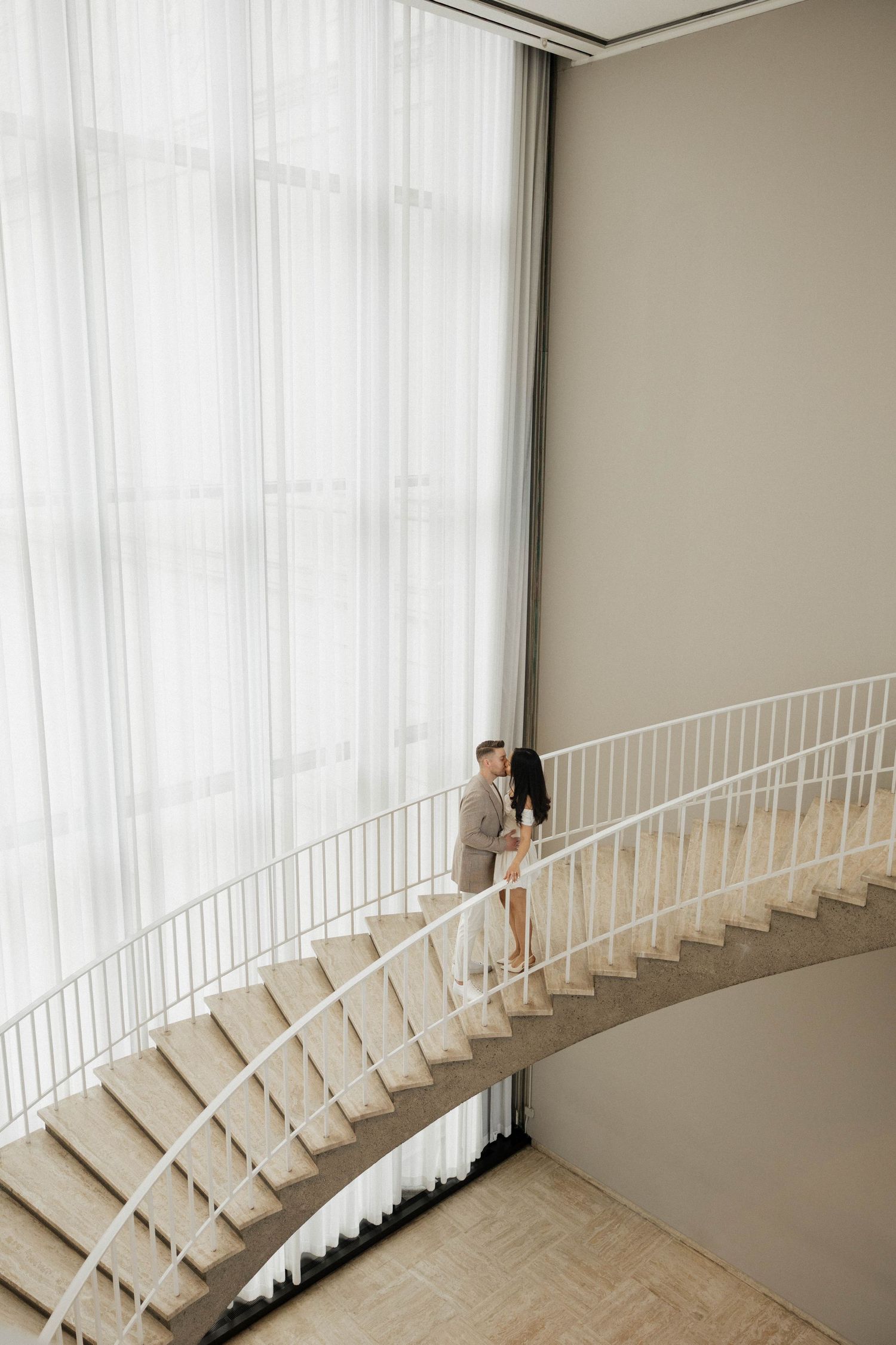 Couple sharing a romantic moment on an elegant curved staircase in a bright modern interior.