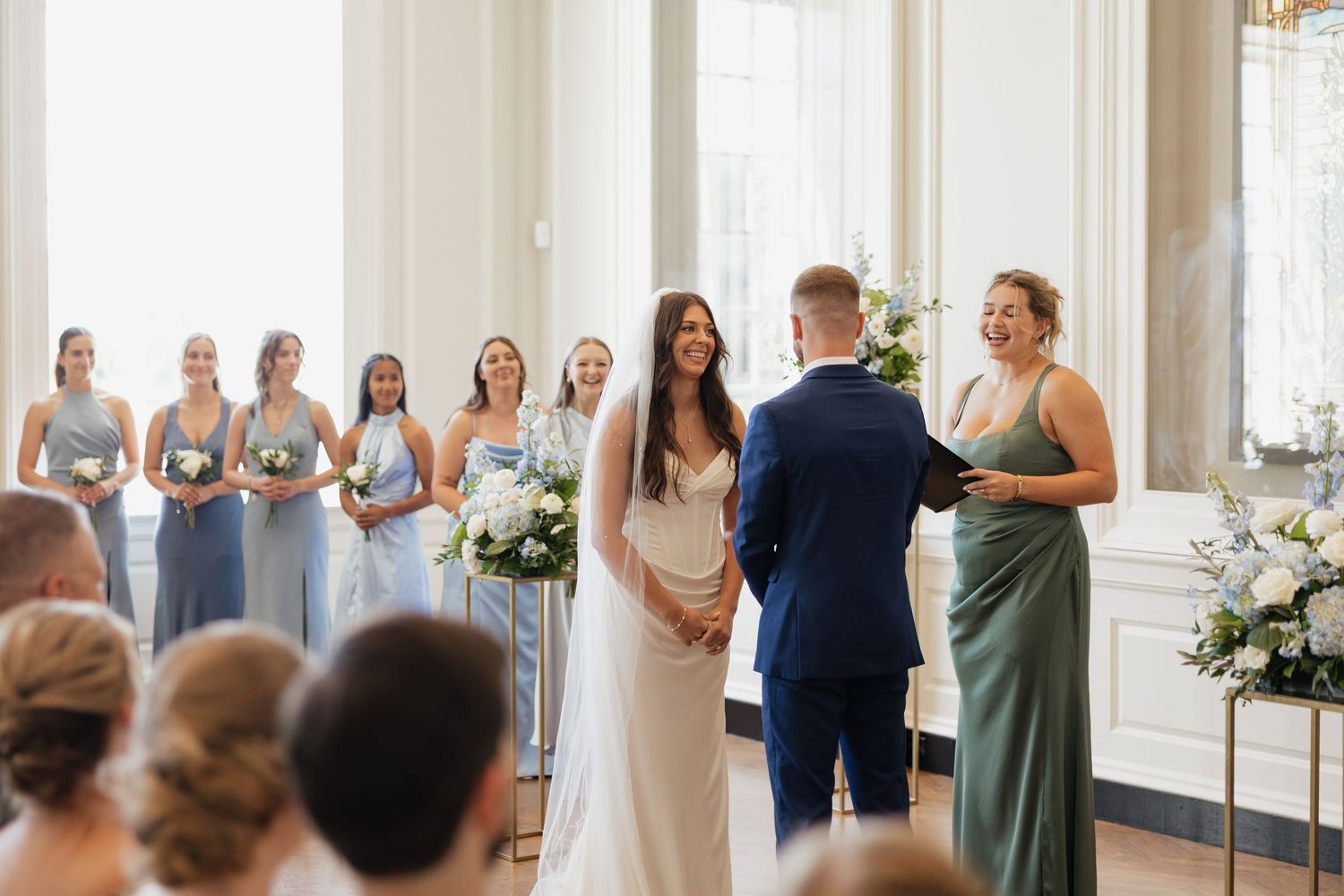 Wedding ceremony guests stand in rows wearing green and gray dresses while watching an emotional moment unfold.