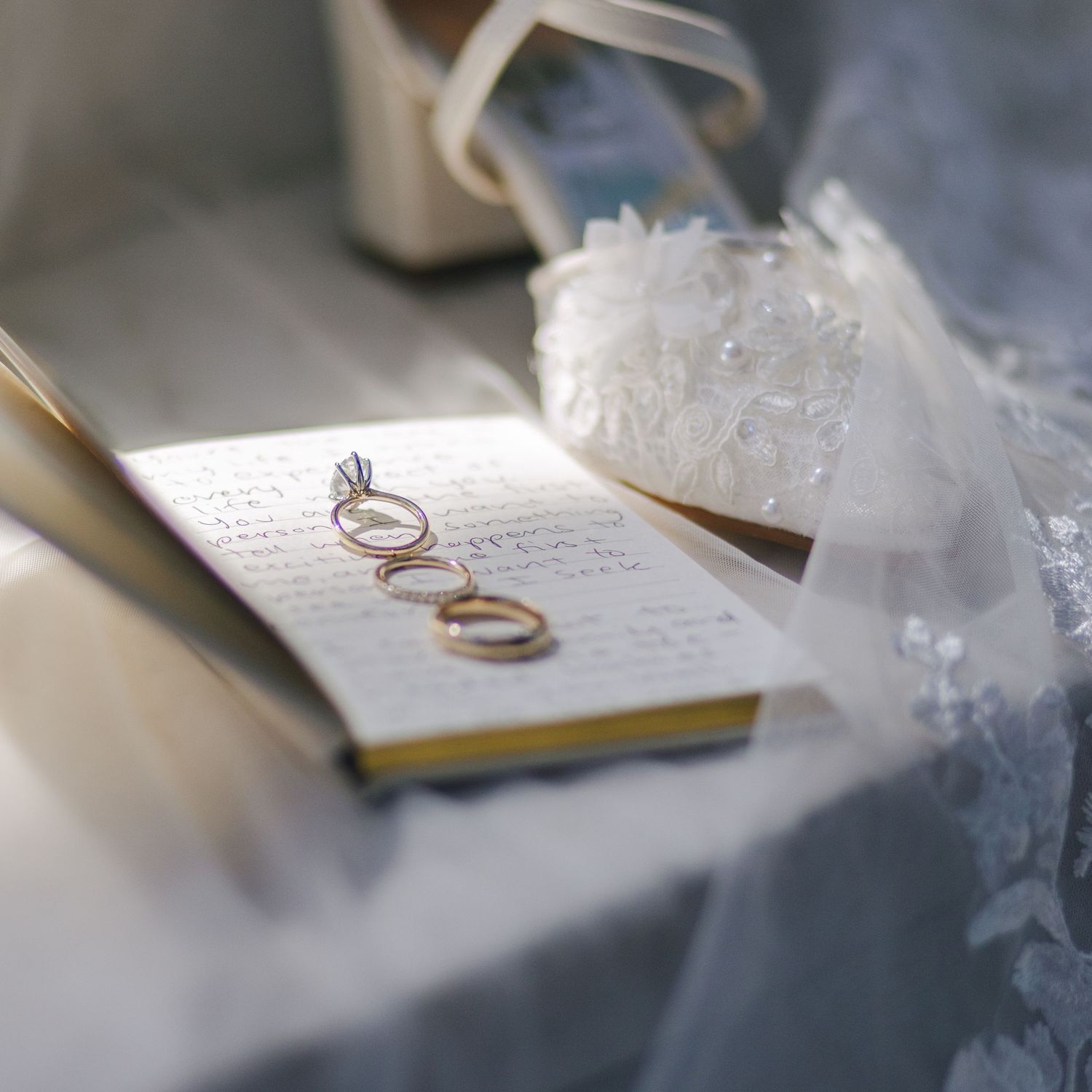 Wedding rings rest on handwritten vows with soft tulle fabric creating a romantic, ethereal backdrop.